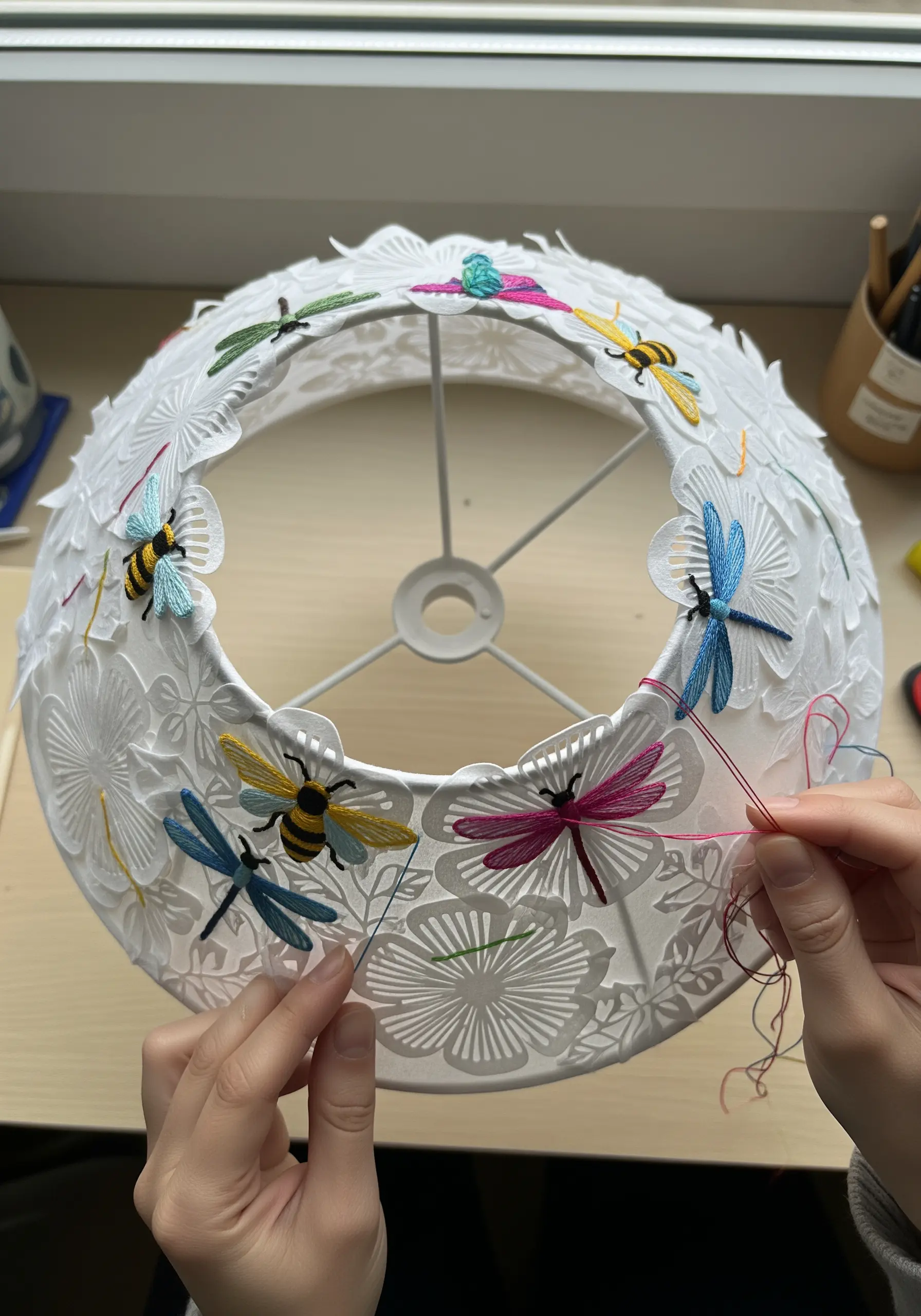 Small, colorful embroidered insects stitched directly onto a white cut-paper lampshade.