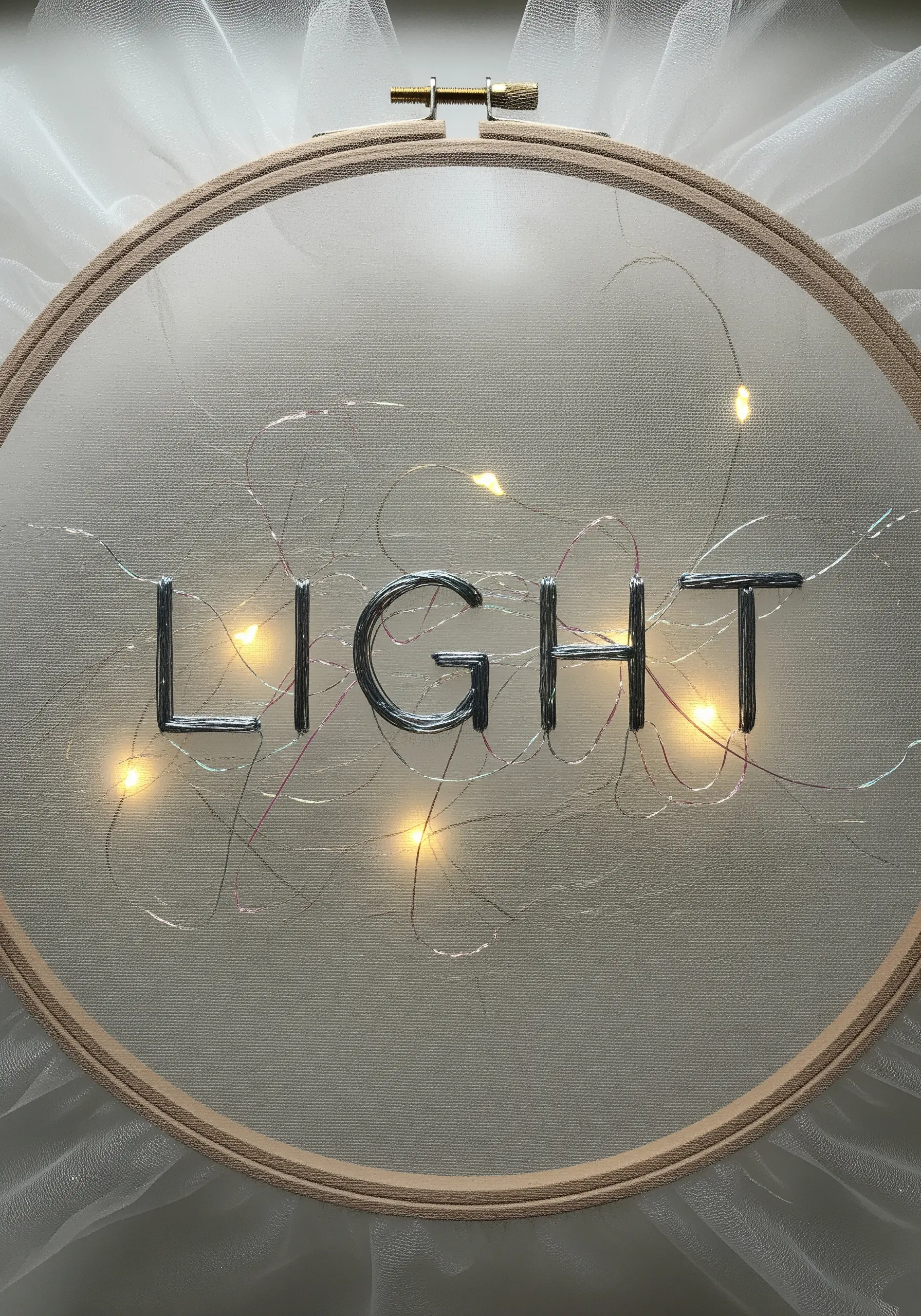 Sheer embroidery hoop with silver thread spelling LIGHT and fairy lights behind
