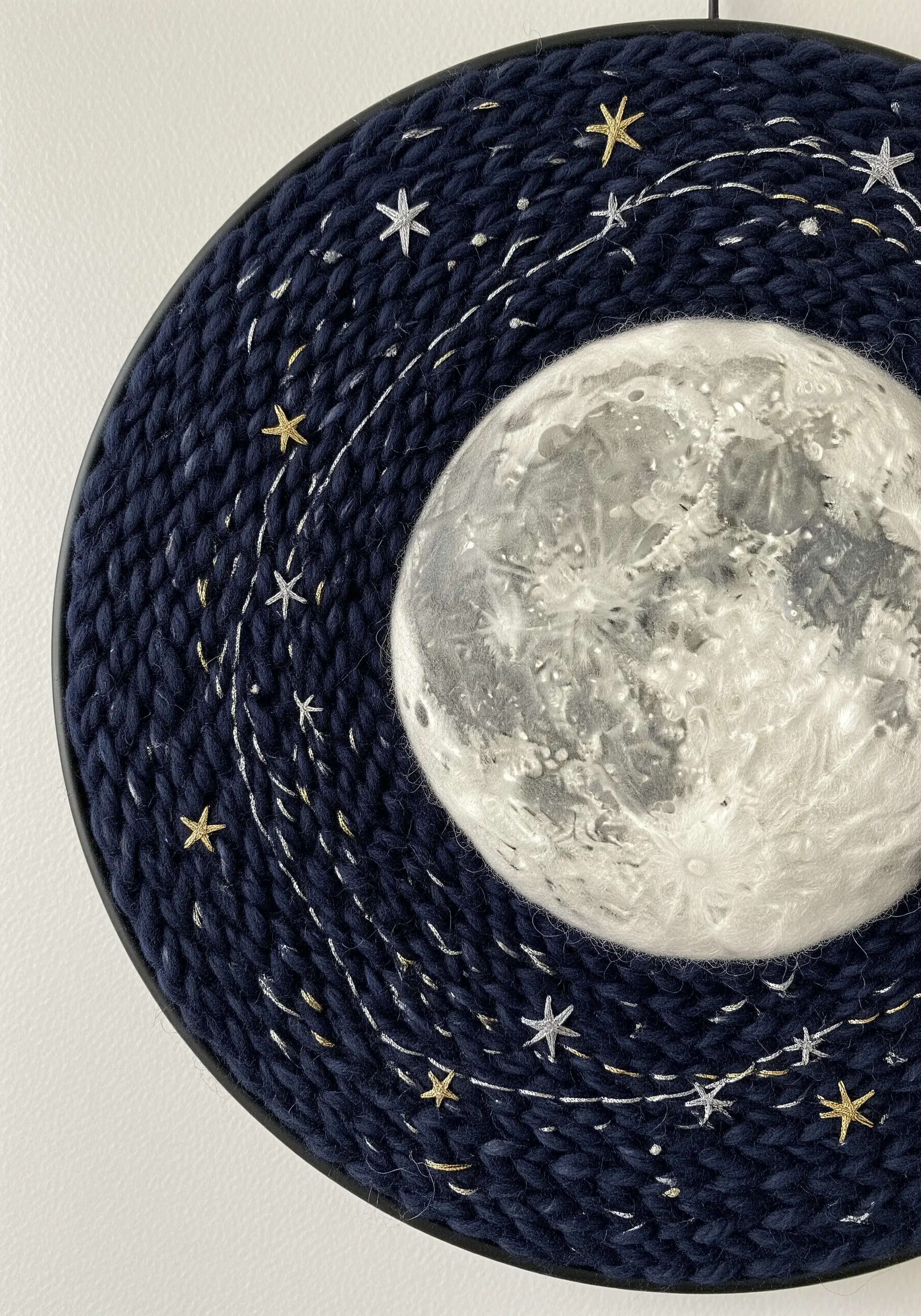 Circular fiber art of a night sky with a felted moon and embroidered metallic stars.