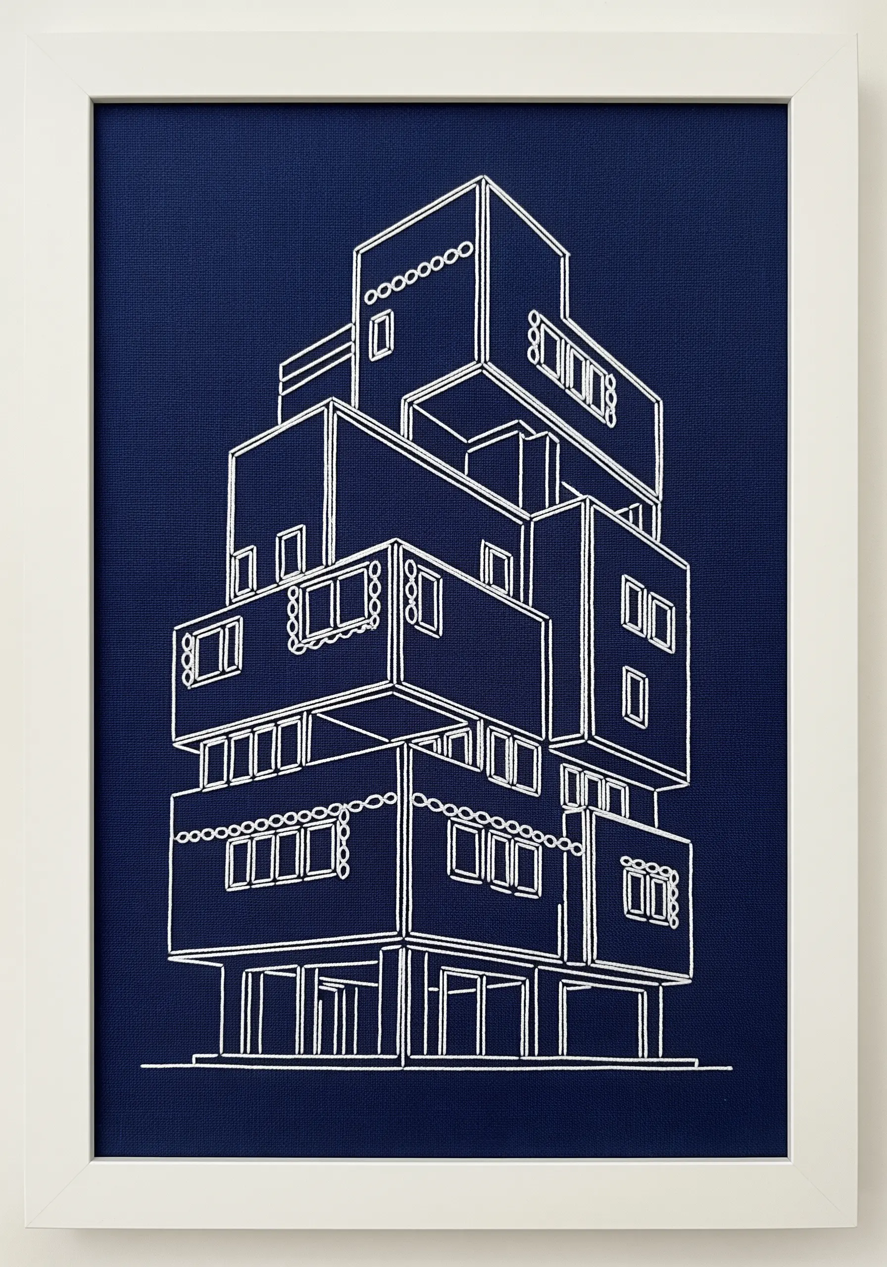 A white-thread line-art embroidery of a stacked, modular building on navy blue fabric.