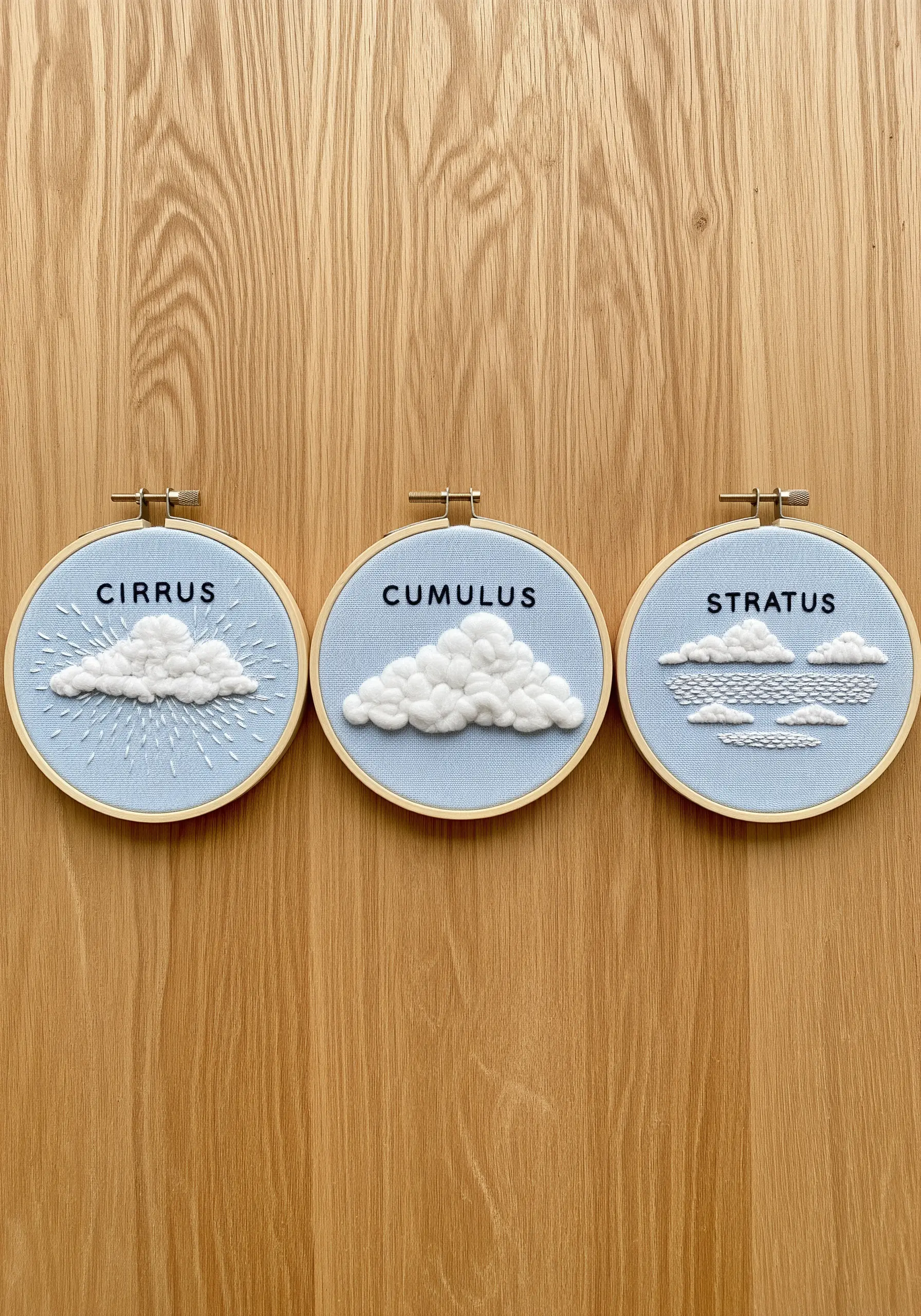 Three embroidery hoops displaying different cloud types: cirrus, cumulus, and stratus.