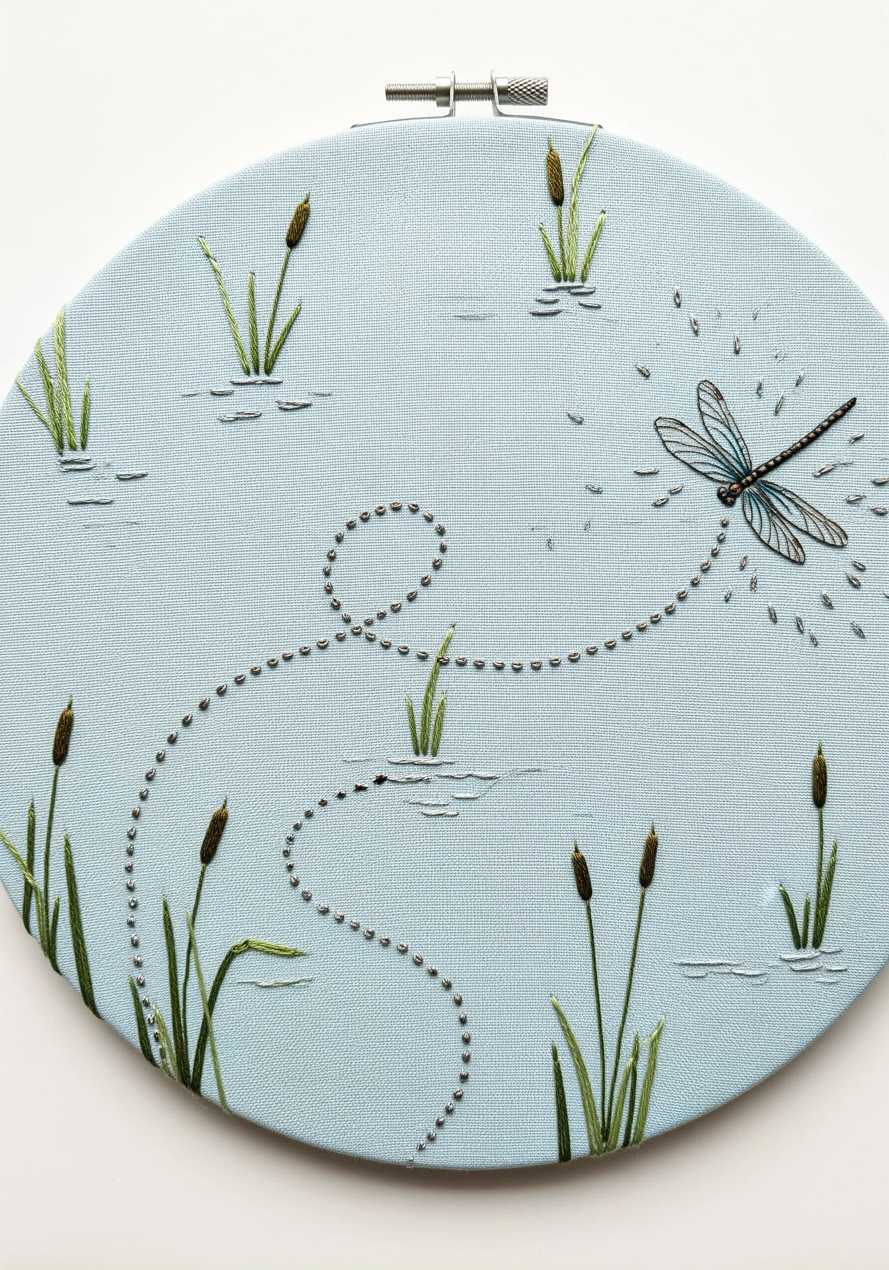 An embroidered dragonfly leaving a swirling trail of silver beads across the fabric.