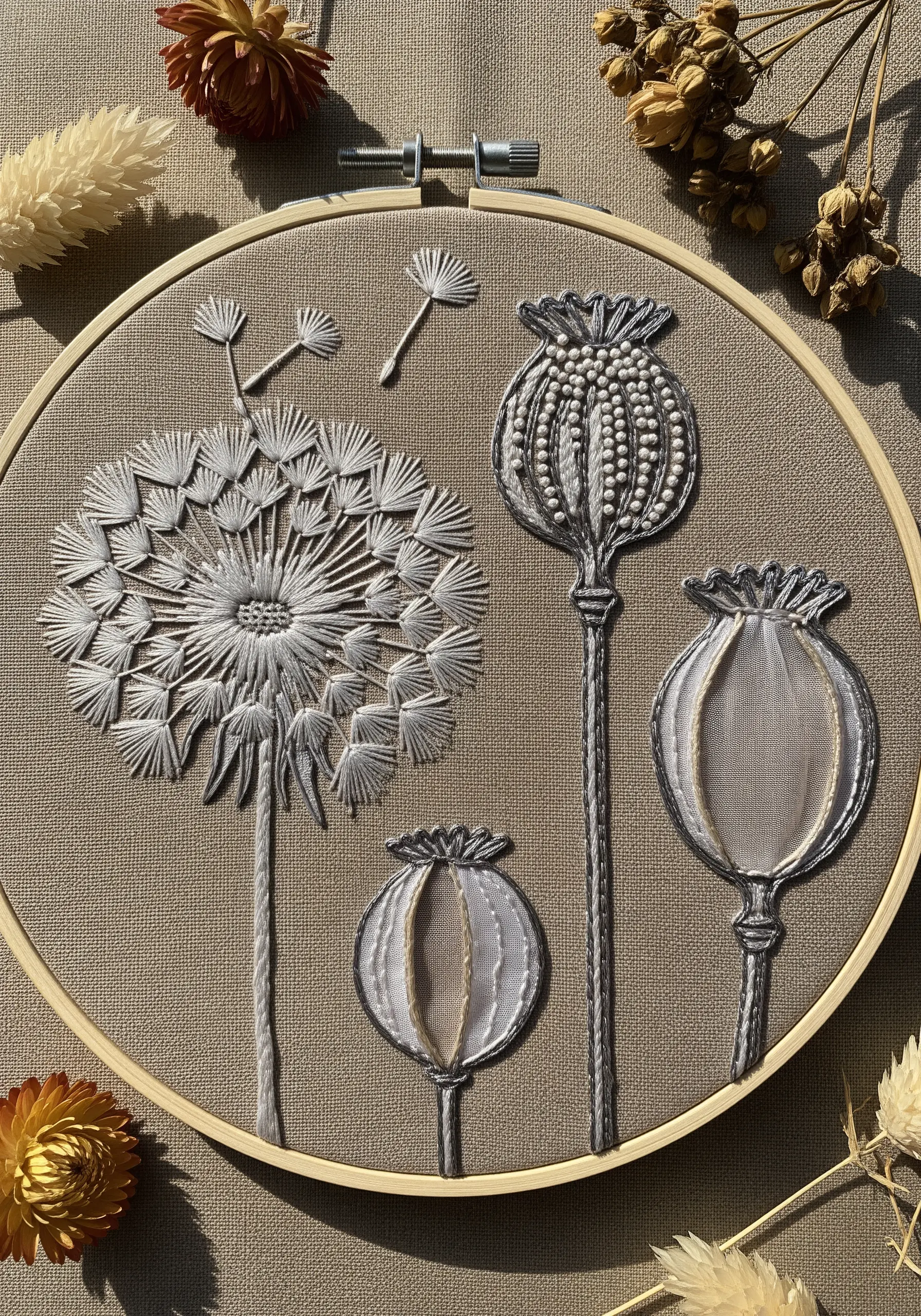 Delicate monochrome embroidery of a dandelion clock and poppy seed heads on brown fabric.