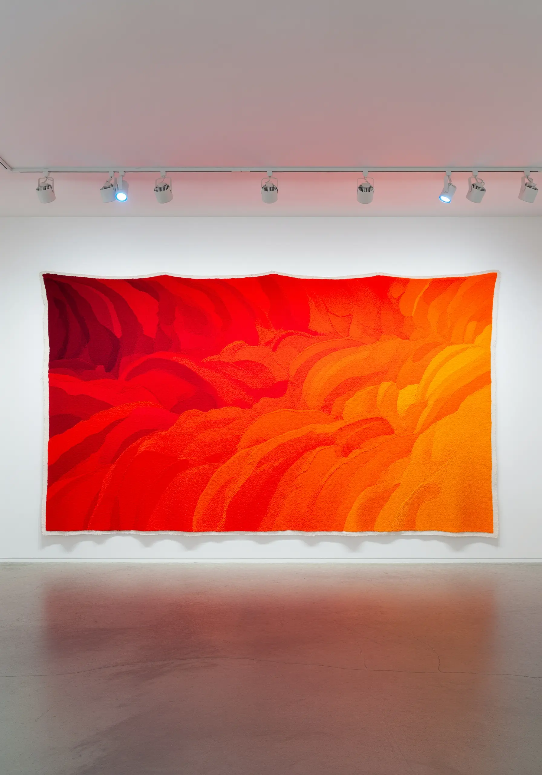 A massive abstract embroidery wall hanging with a vibrant red-to-orange gradient.