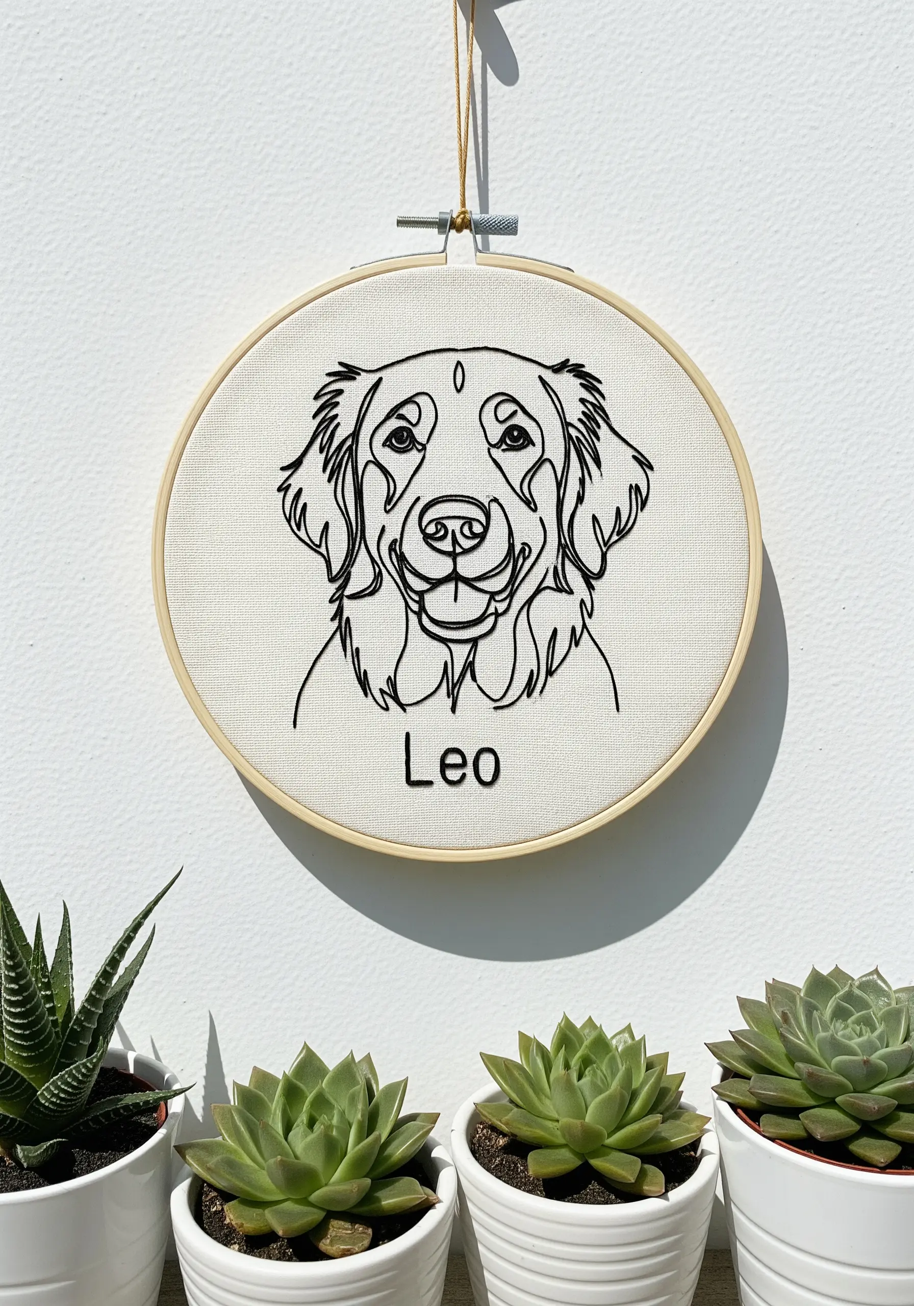 A minimalist line art portrait of a golden retriever embroidered in black thread in a hoop.