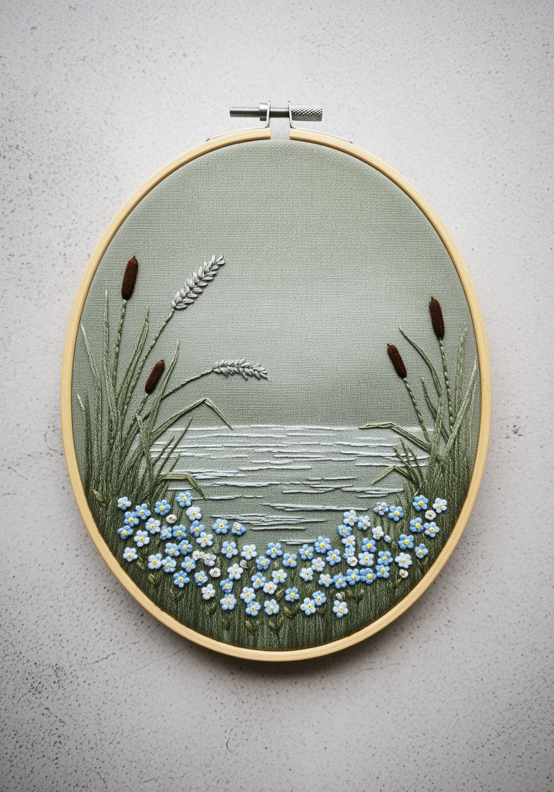 A serene pond scene embroidered on sage green fabric, with forget-me-nots in the foreground.