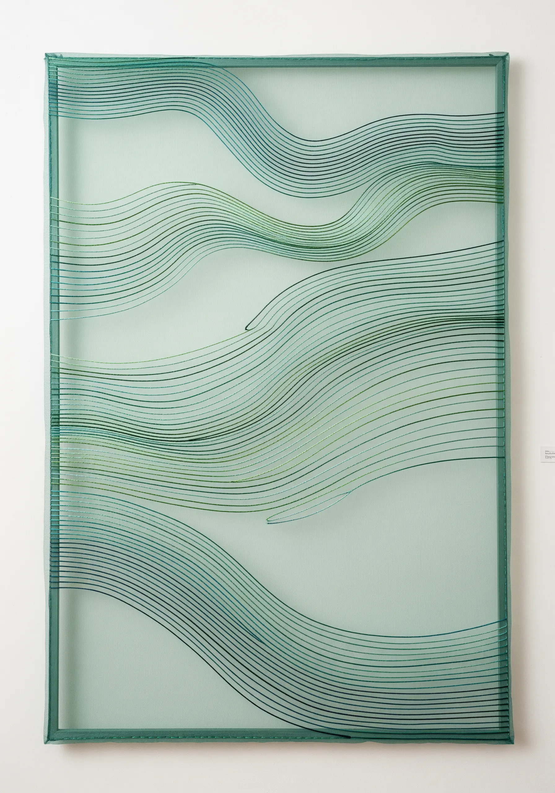 Wavy green and blue lines stitched on transparent fabric, creating layers of color.
