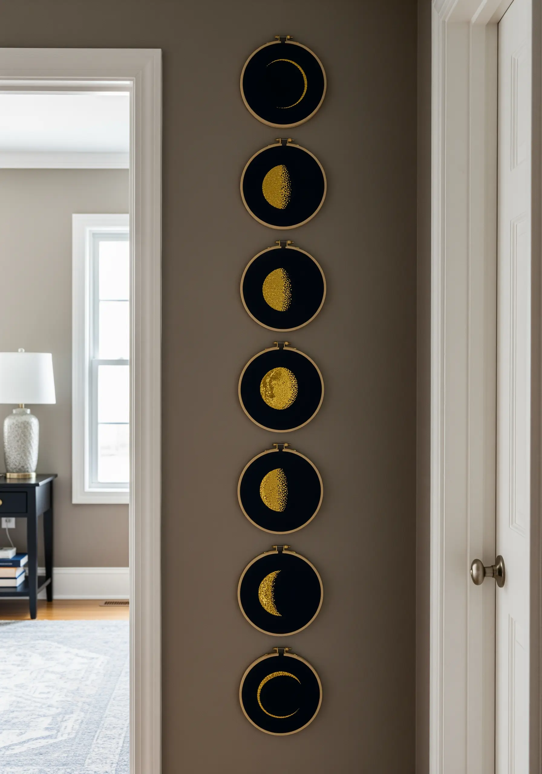 A vertical series of seven embroidery hoops showing moon phases filled with gold seed stitches.