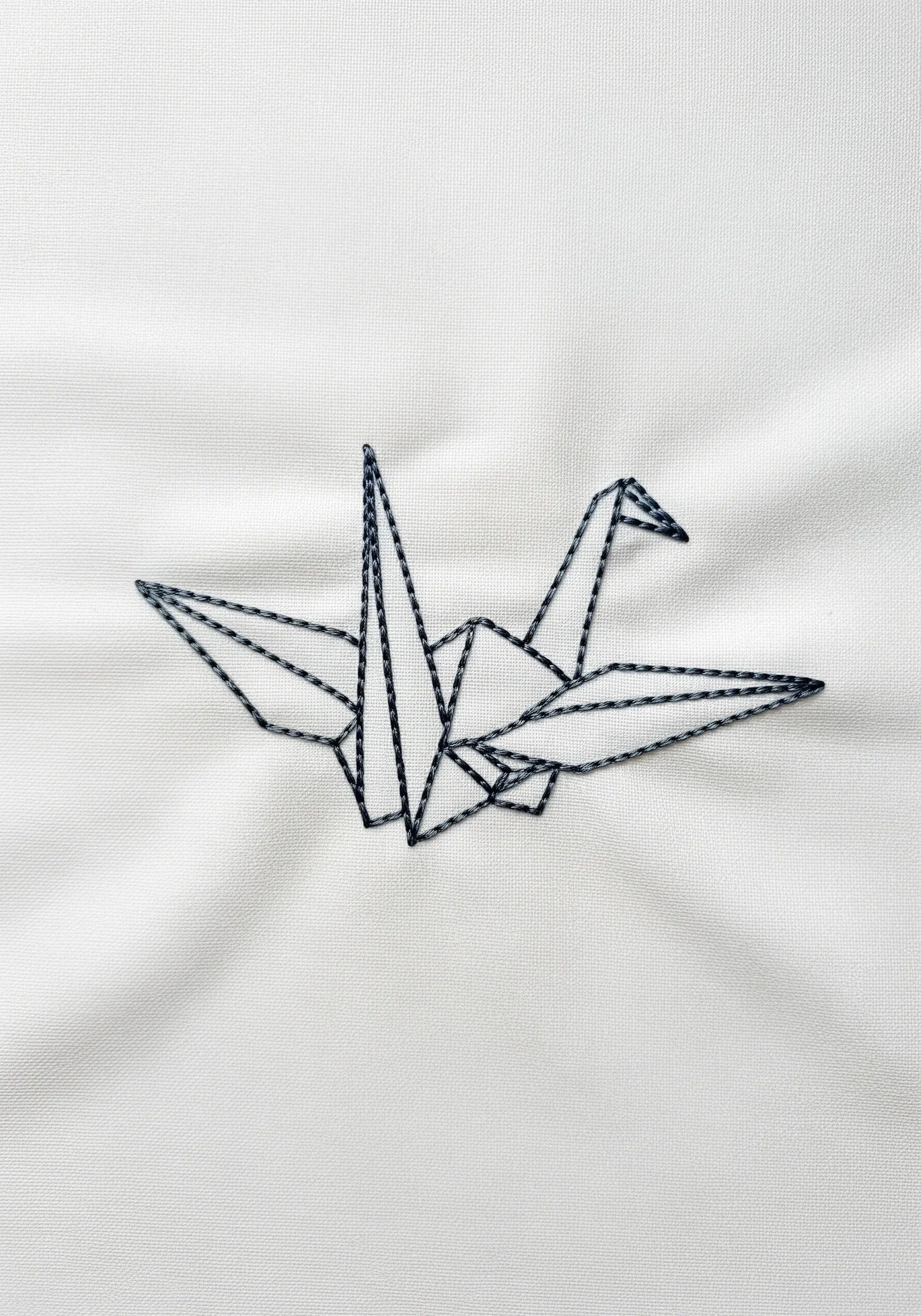 A geometric origami crane embroidered with a dark grey backstitch on white fabric.