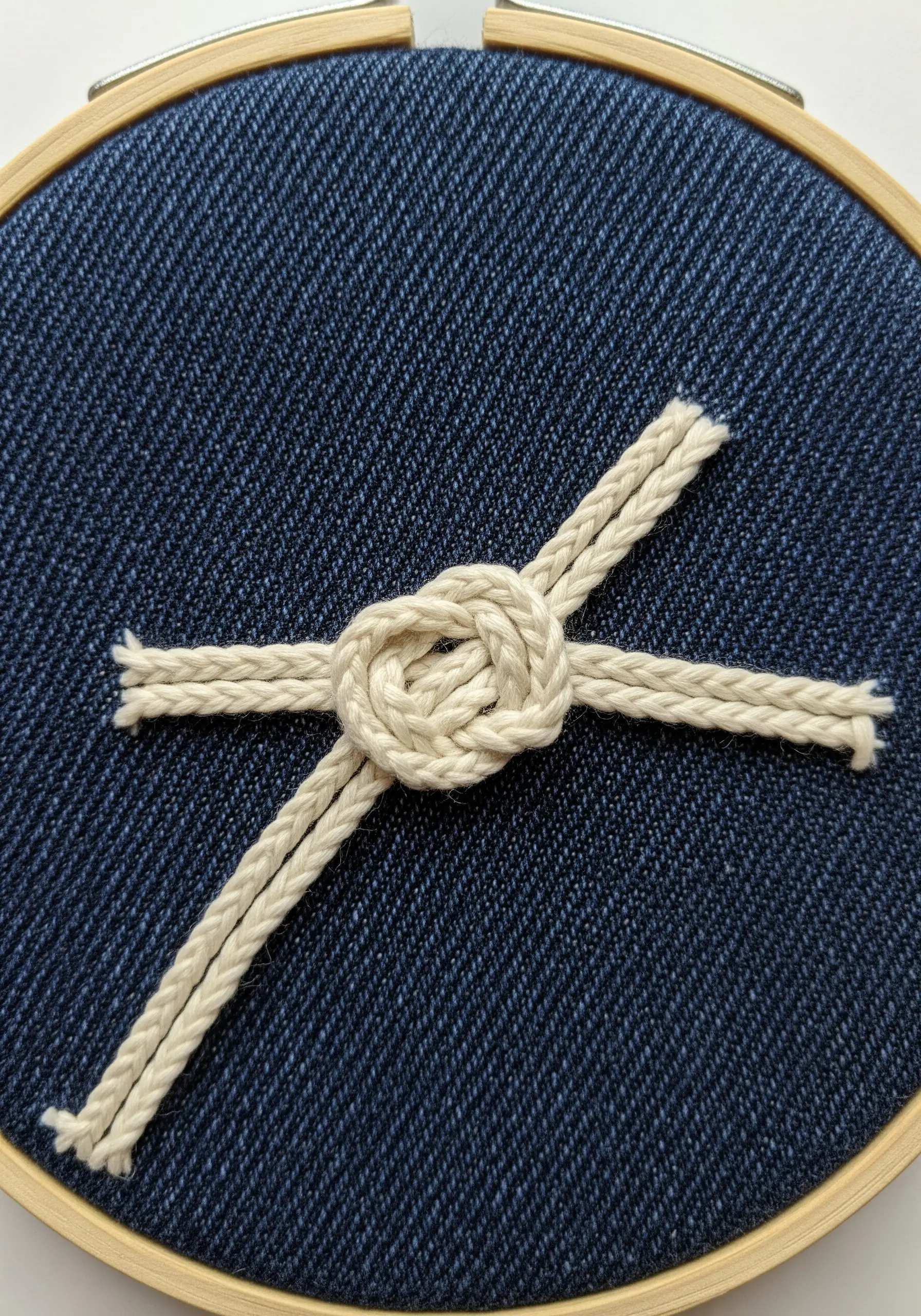 A rope knot stitched onto dark denim fabric in a hoop.
