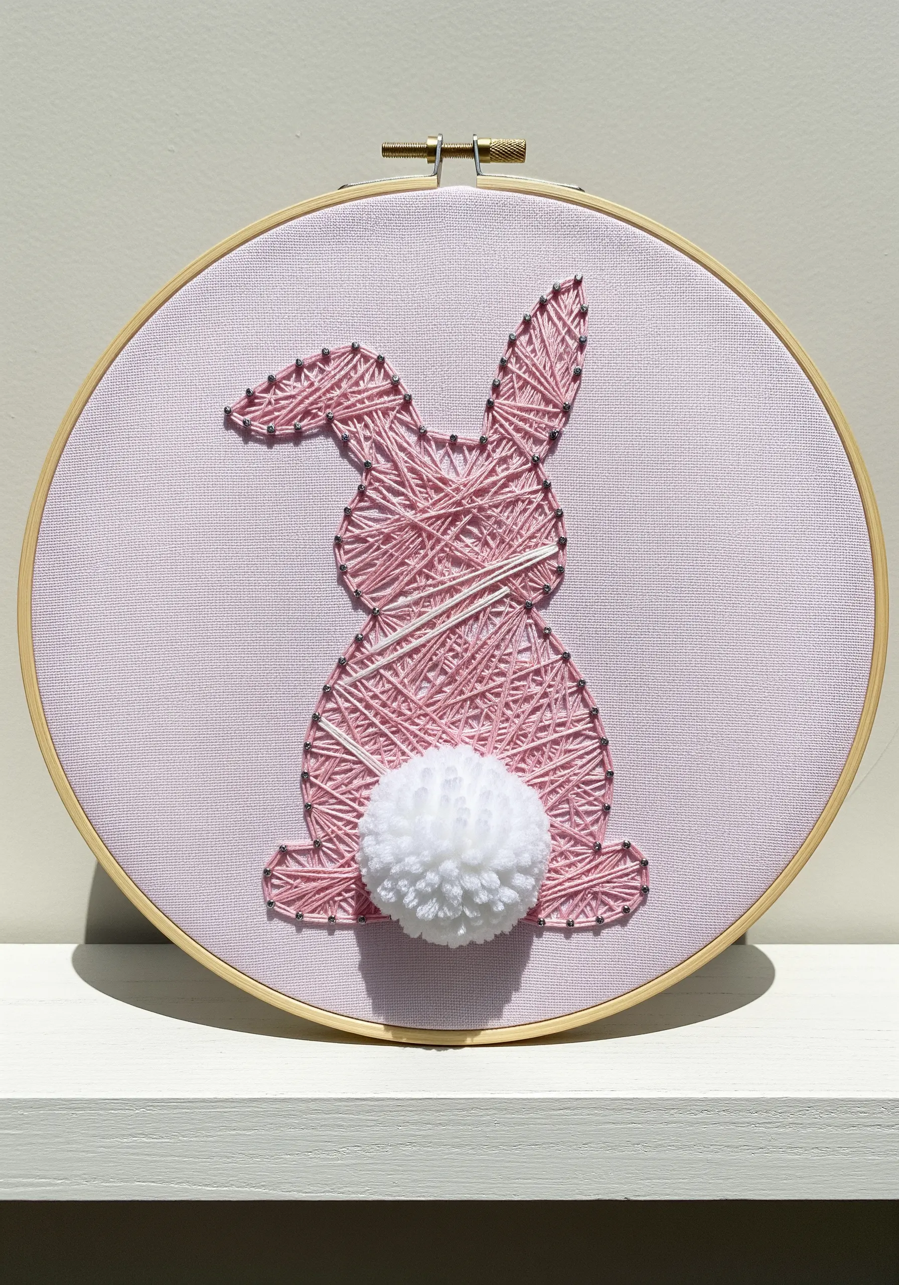 Pink string art style embroidery of a rabbit with a white yarn pom-pom tail.