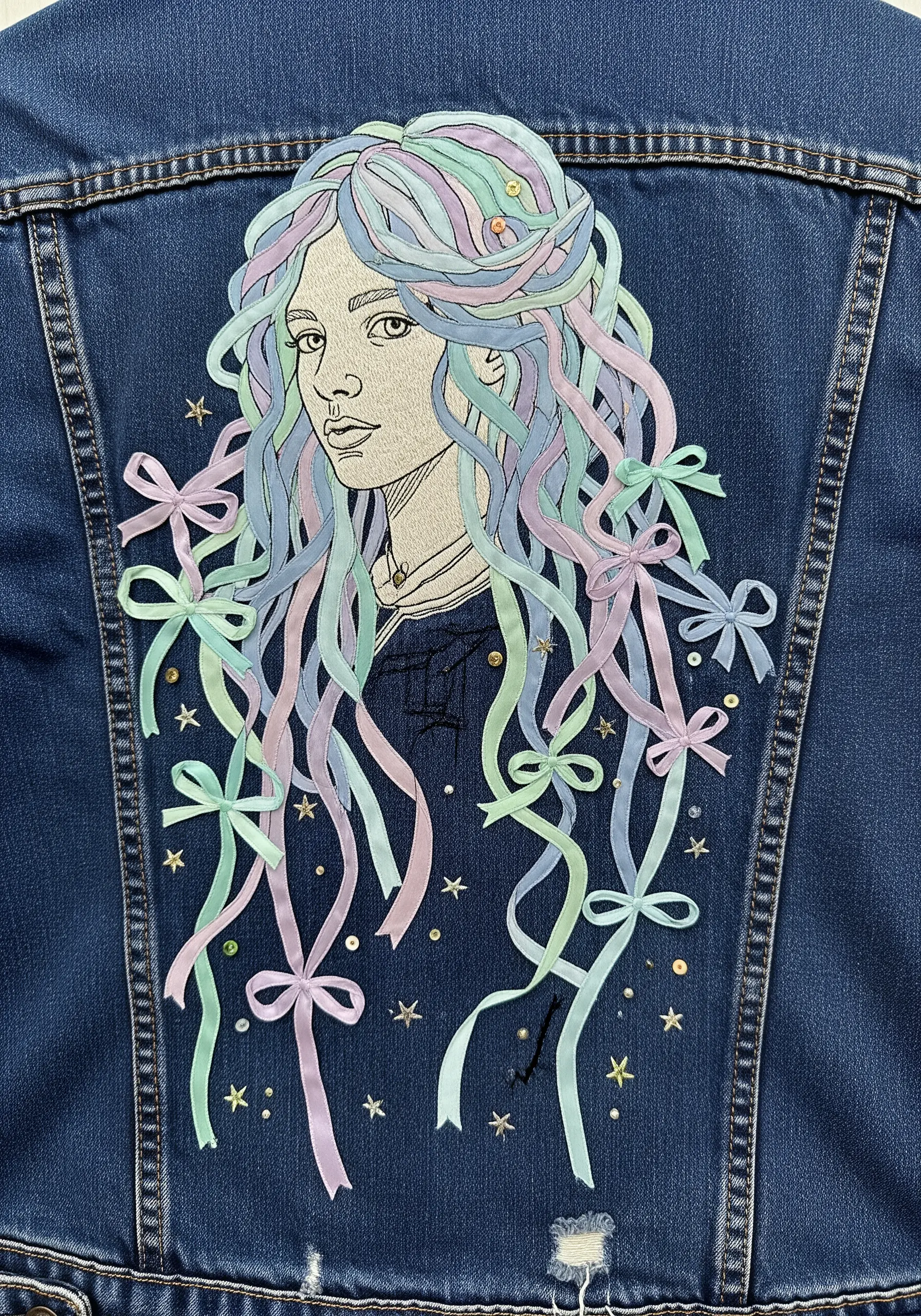 Embroidered portrait with pastel-colored ribbons forming long, flowing hair decorated with bows.