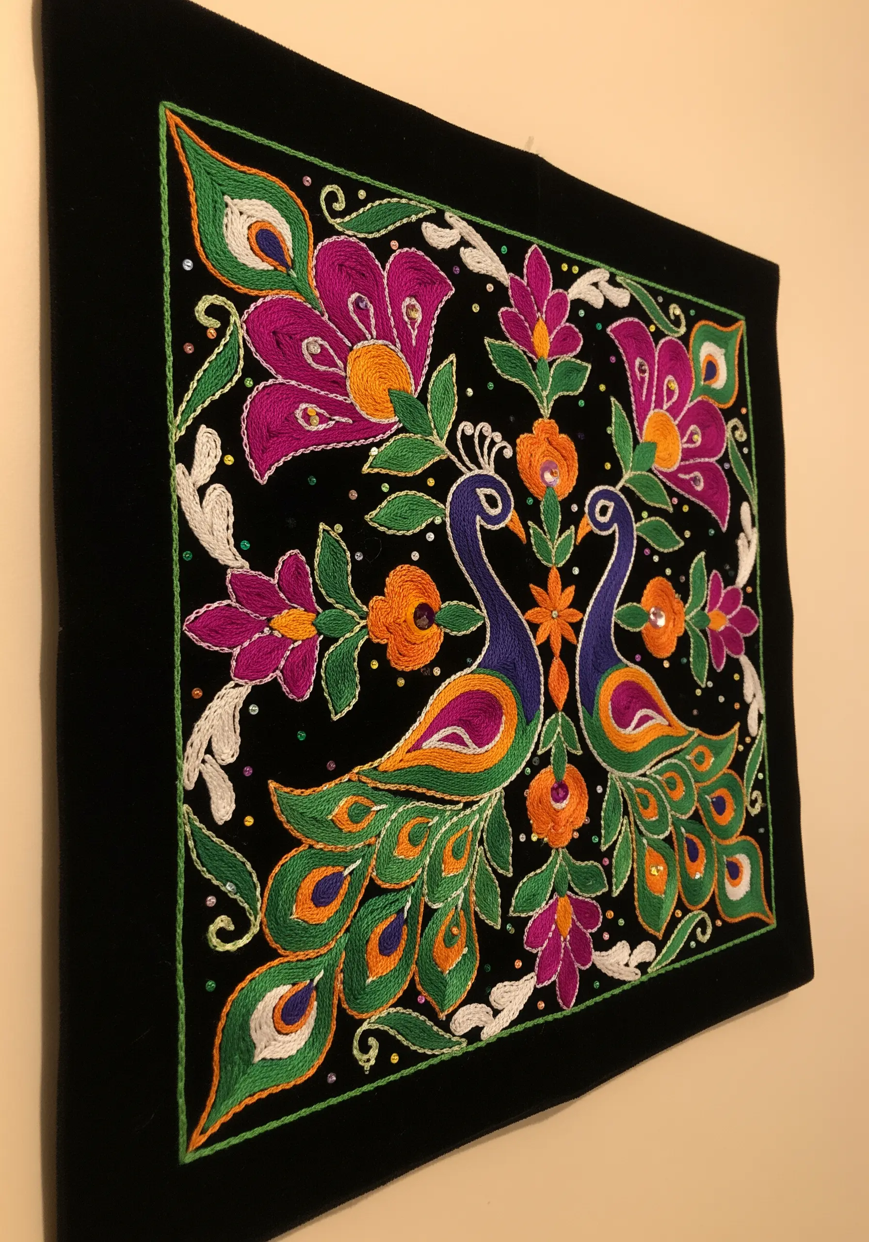 Indian-inspired embroidery of two peacocks with vibrant magenta, orange, and green threads.