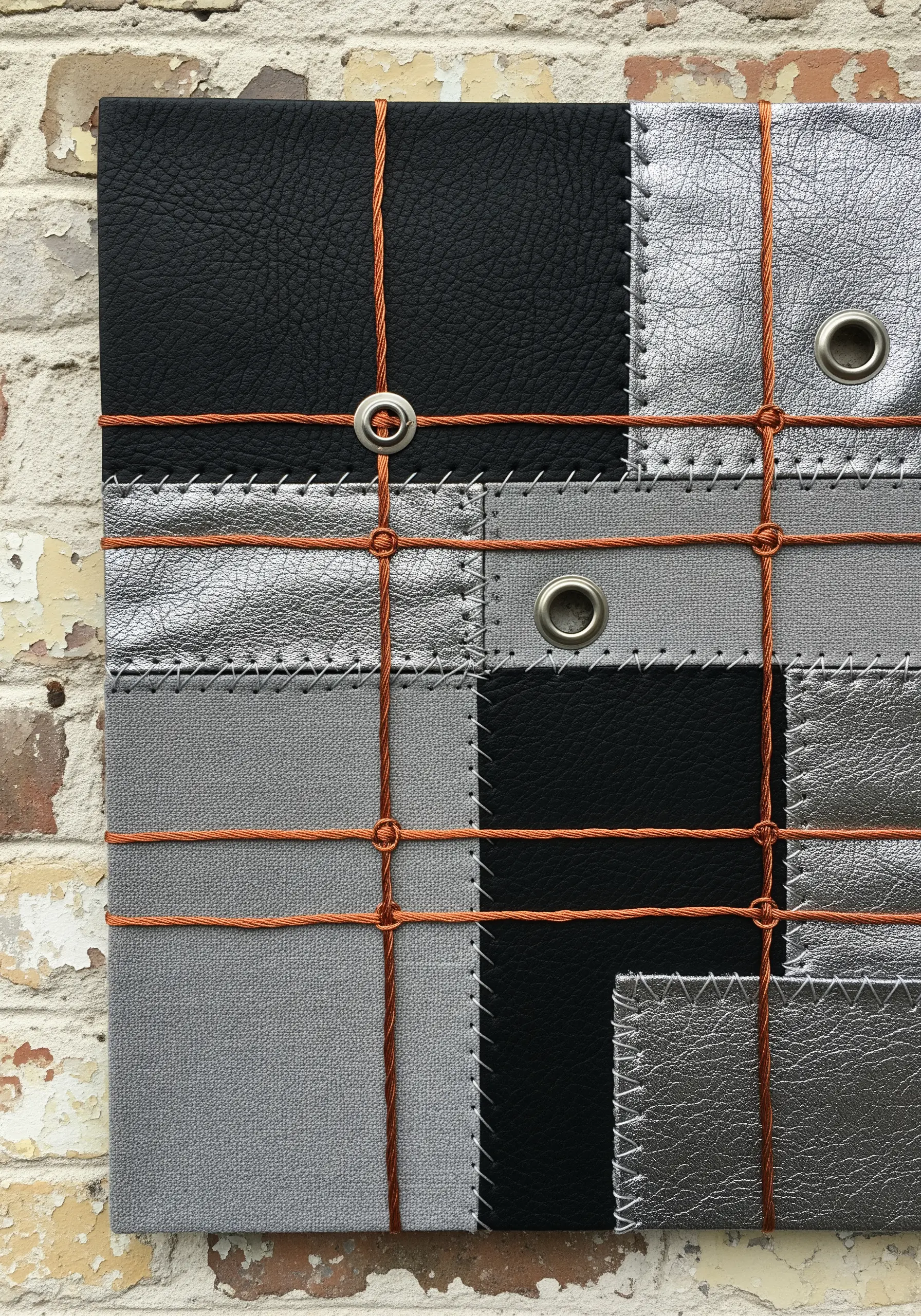 A patchwork of black and silver leather scraps with orange cord laced through metal grommets.