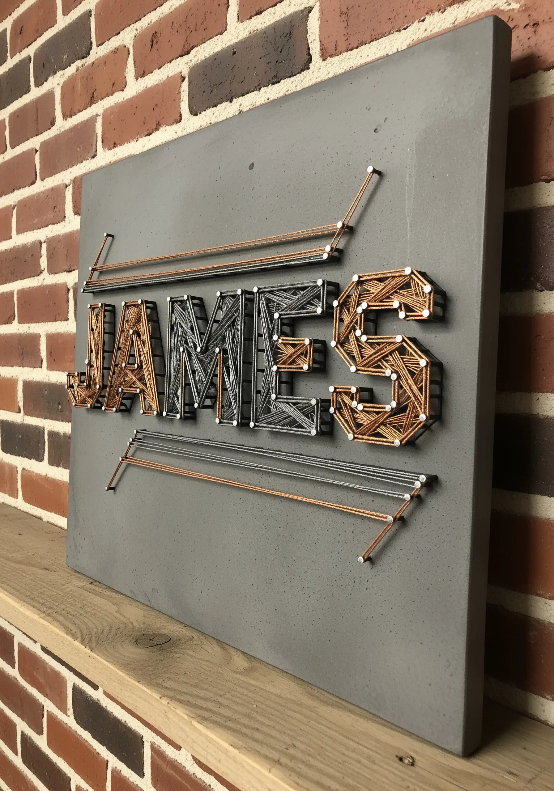 Industrial-style name embroidery with metallic threads on a gray concrete-like board.