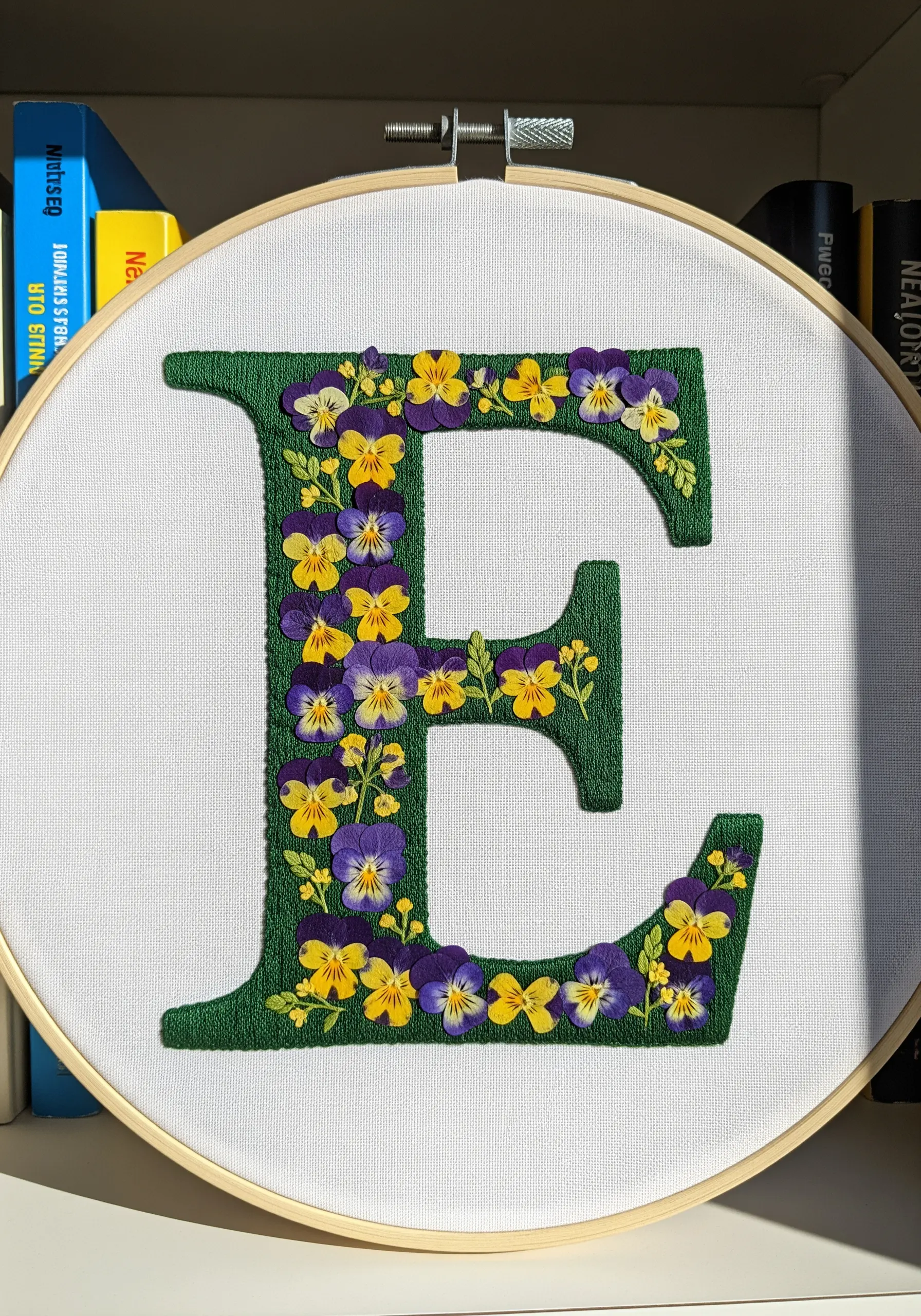 Satin-stitched letter 'E' filled with tiny pressed pansies and violas.