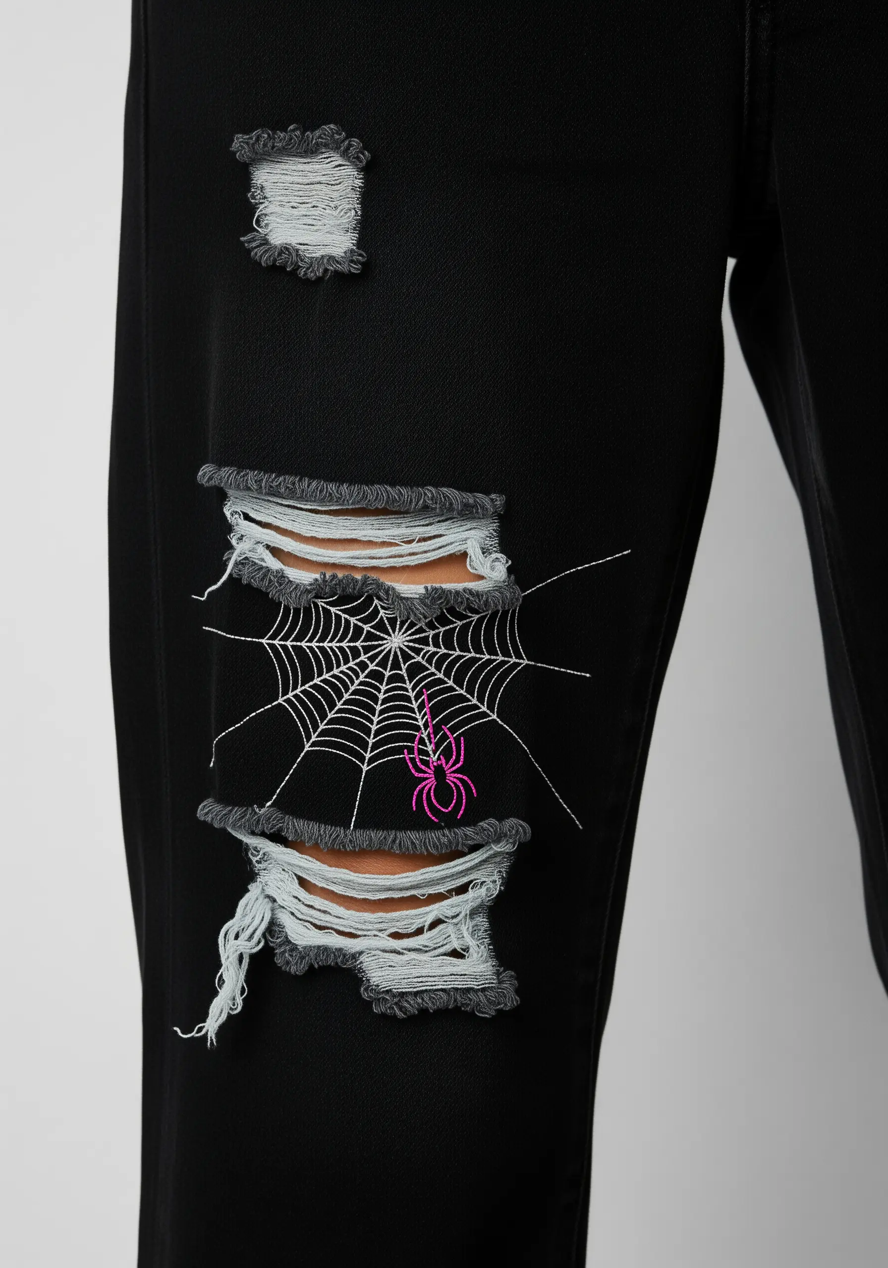 A delicate spiderweb embroidered over a rip in black jeans, with a small neon pink spider.