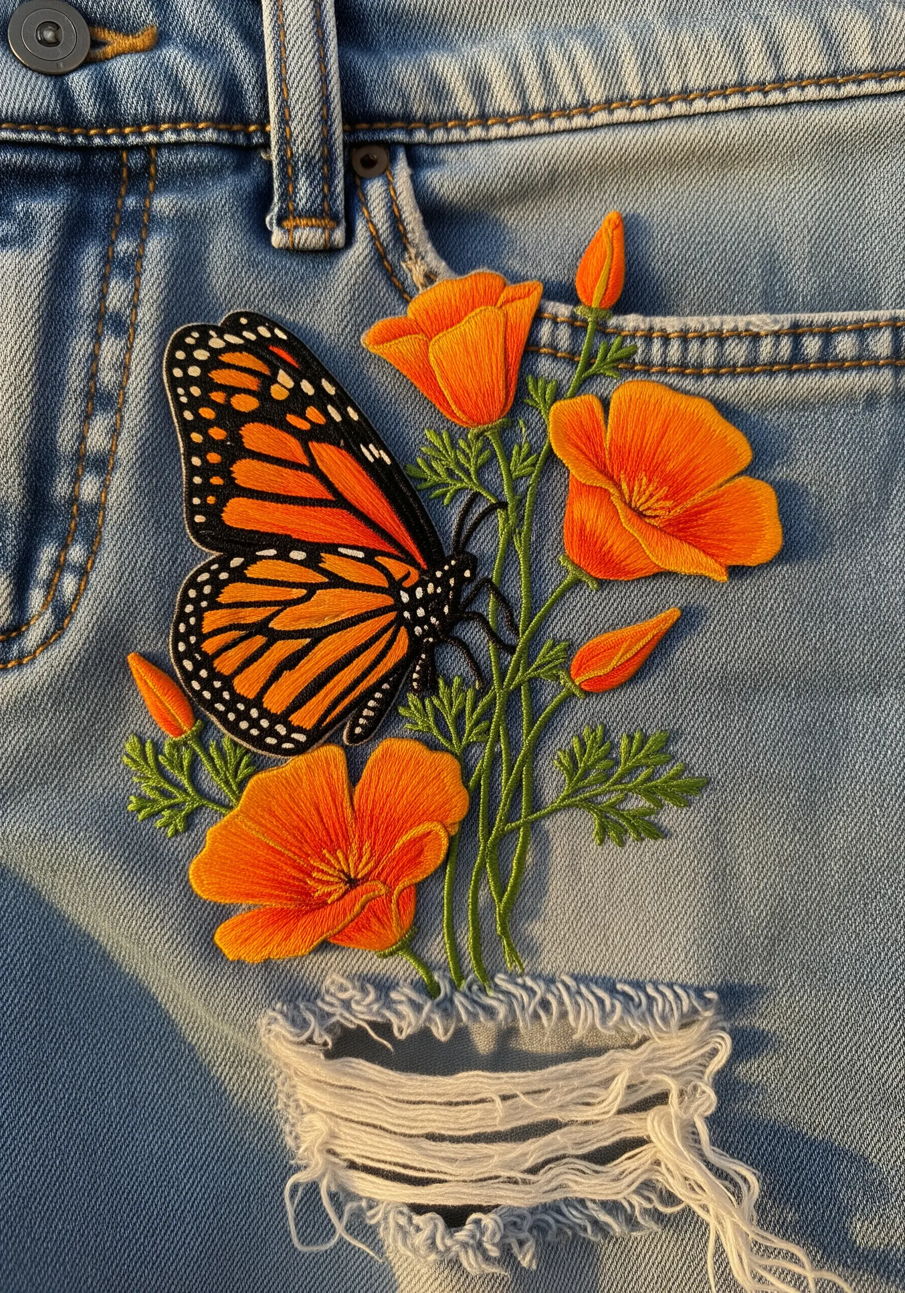 A monarch butterfly and orange poppies embroidered to look like they're growing from ripped denim.