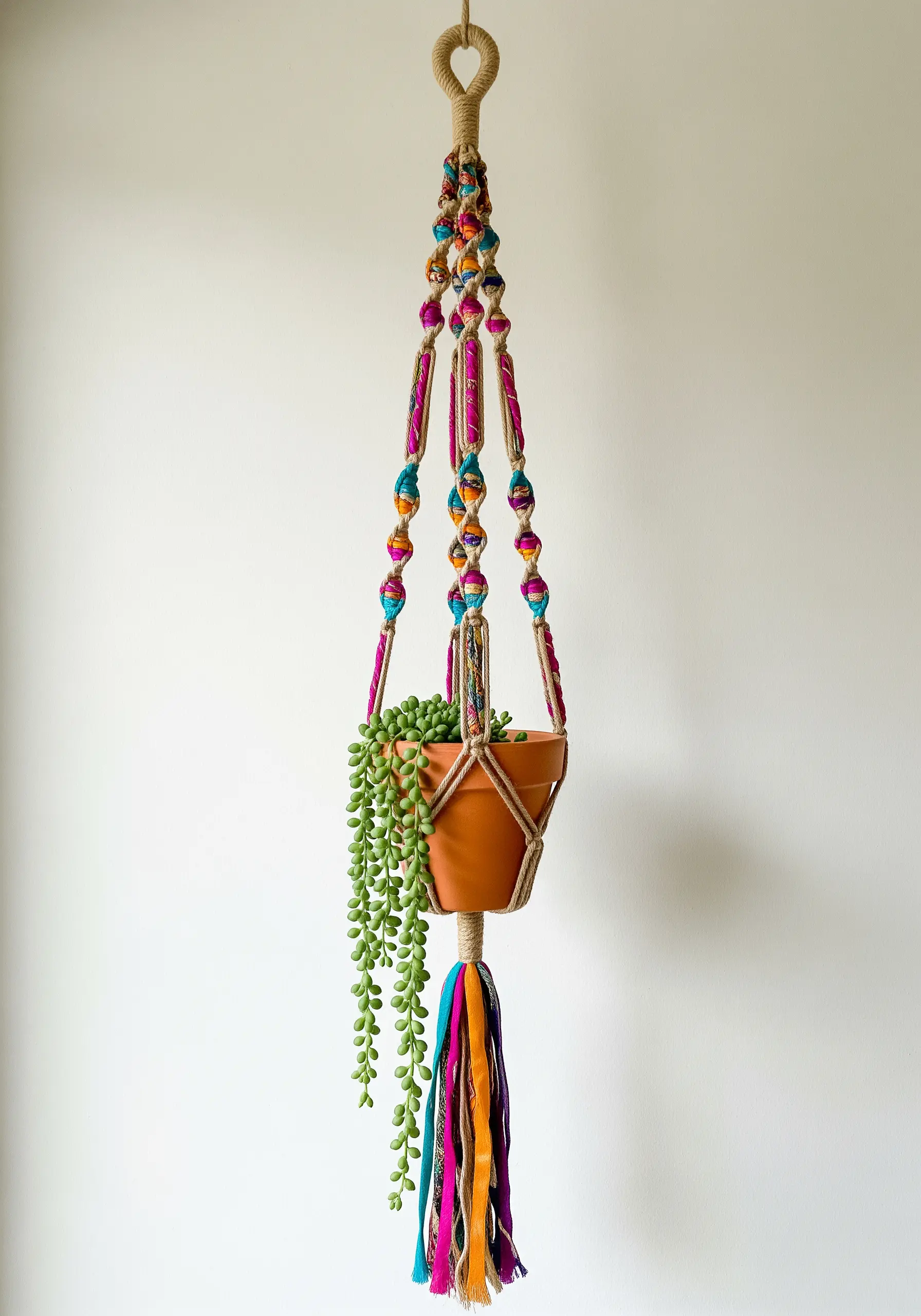 Macrame plant hanger made with jute and colorful patterned fabric strips holding a potted plant.