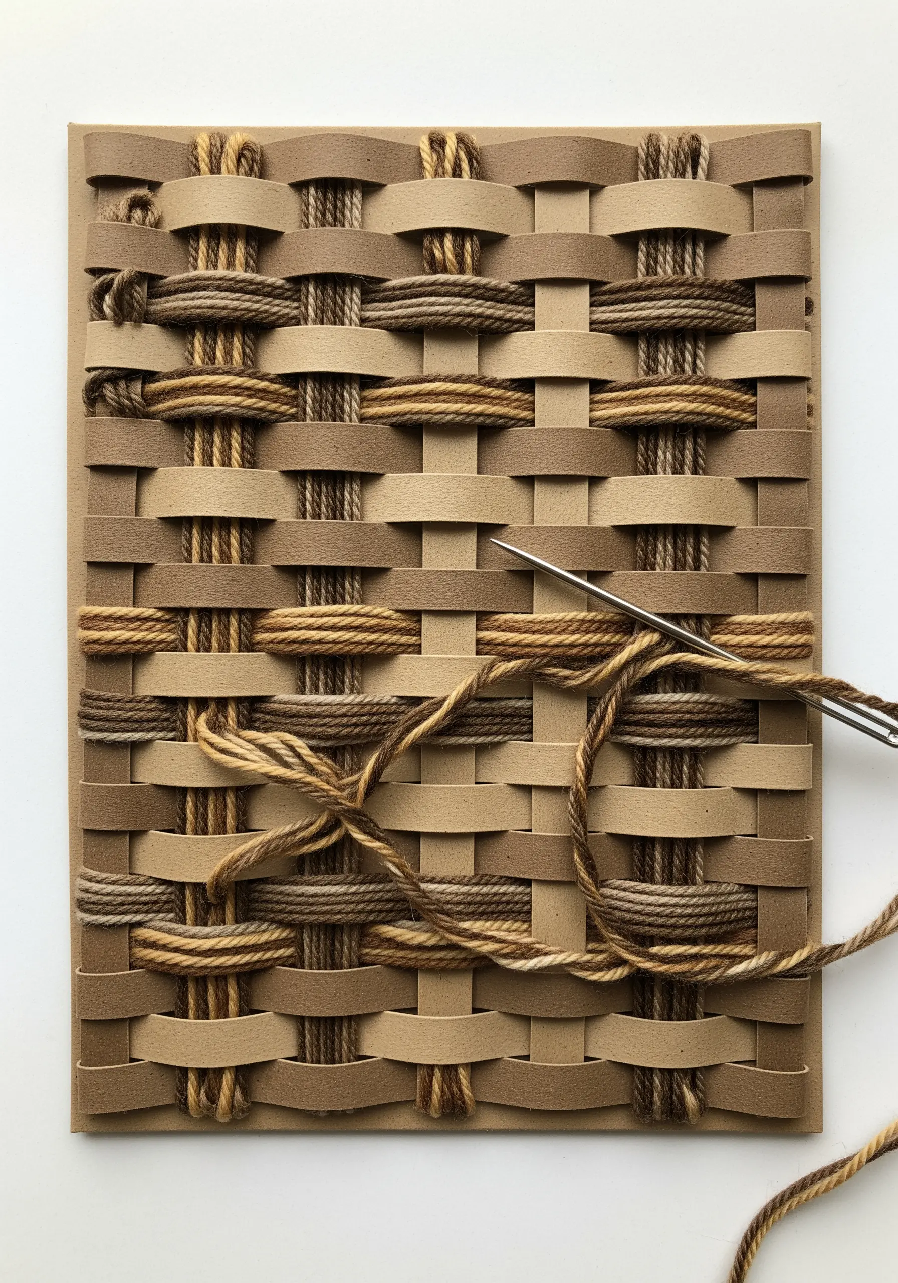 Yarn being woven through a grid of woven brown and tan paper strips.
