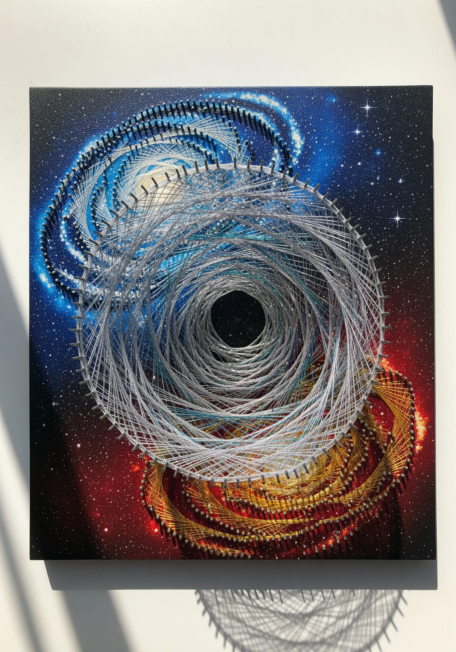 String art of two overlapping spiral galaxies, one blue and one gold, on a painted nebula canvas.