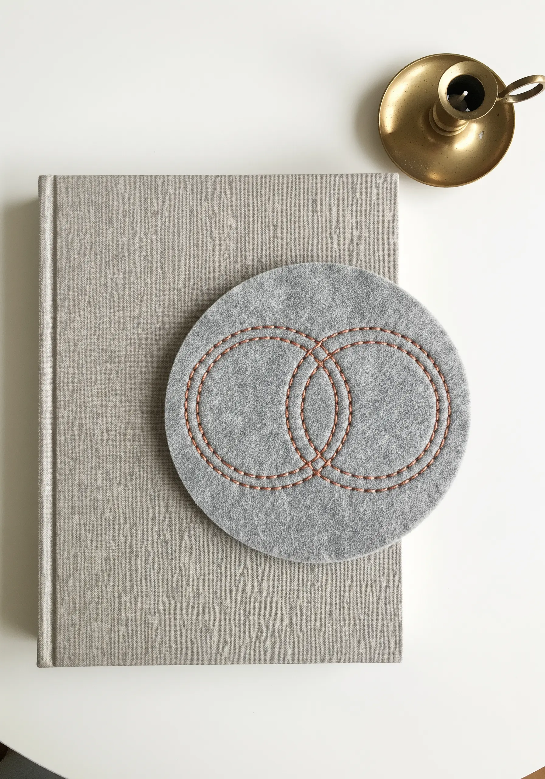 Two interlocking circles stitched in brown thread on a round grey felt coaster.