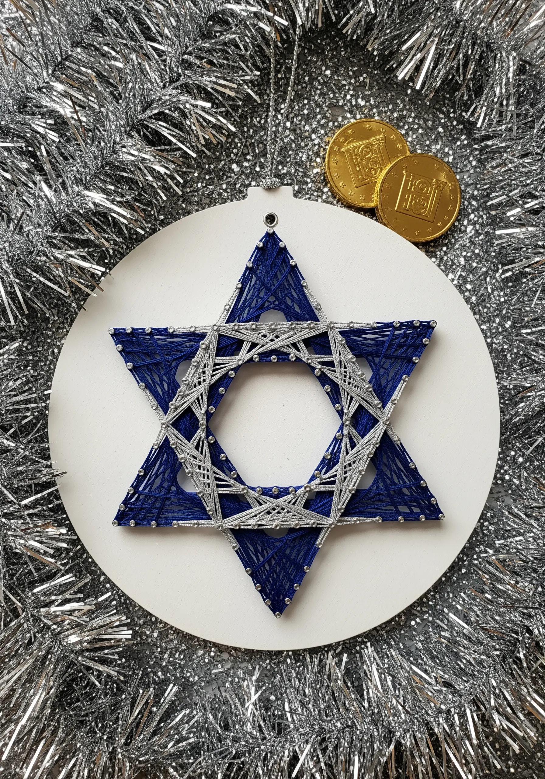 Blue and silver string art Star of David on a white circular ornament.