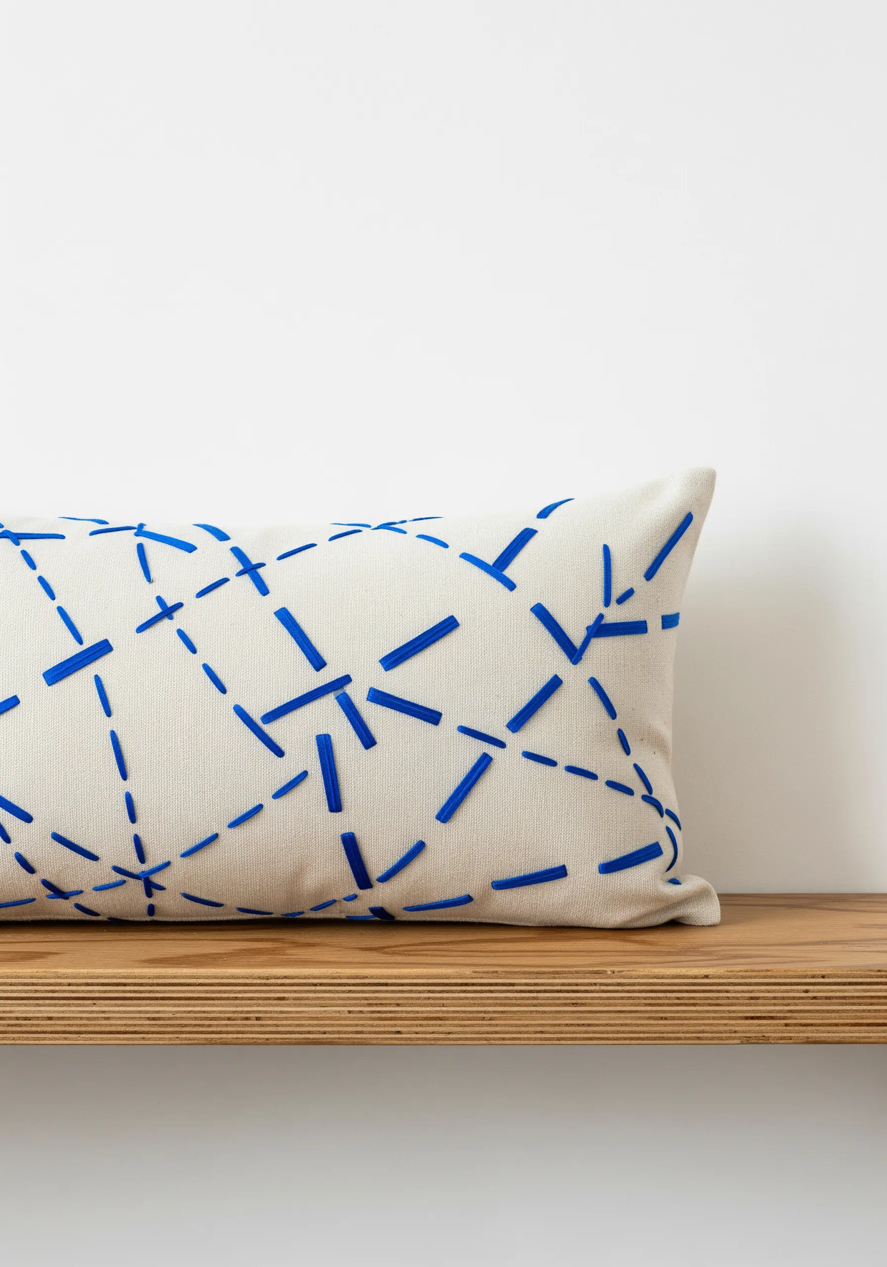 A geometric pattern of bold blue satin stitch bars creating dashed lines on a cream pillow.