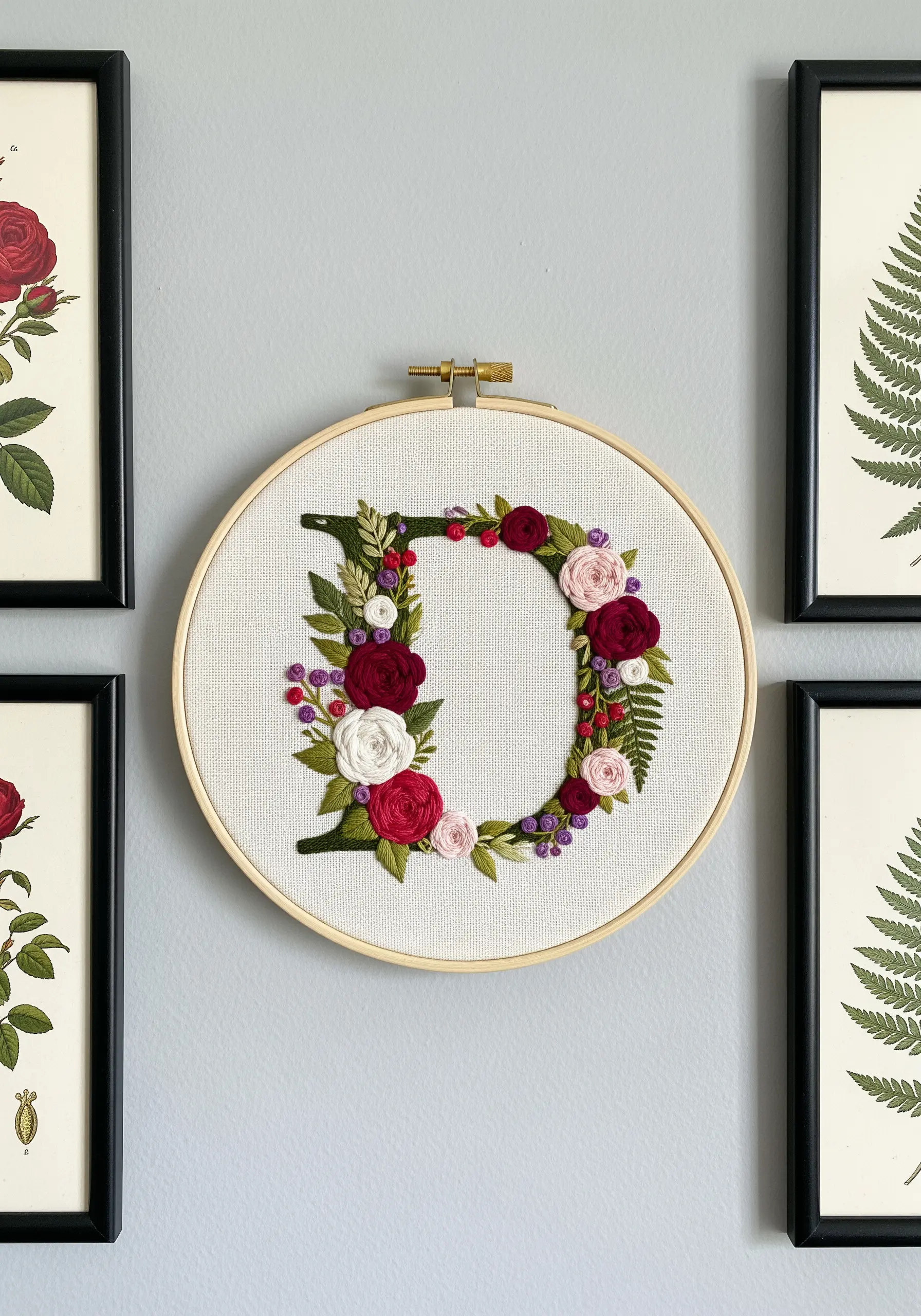 Embroidery hoop with letter D formed by vines, red roses, and green ferns