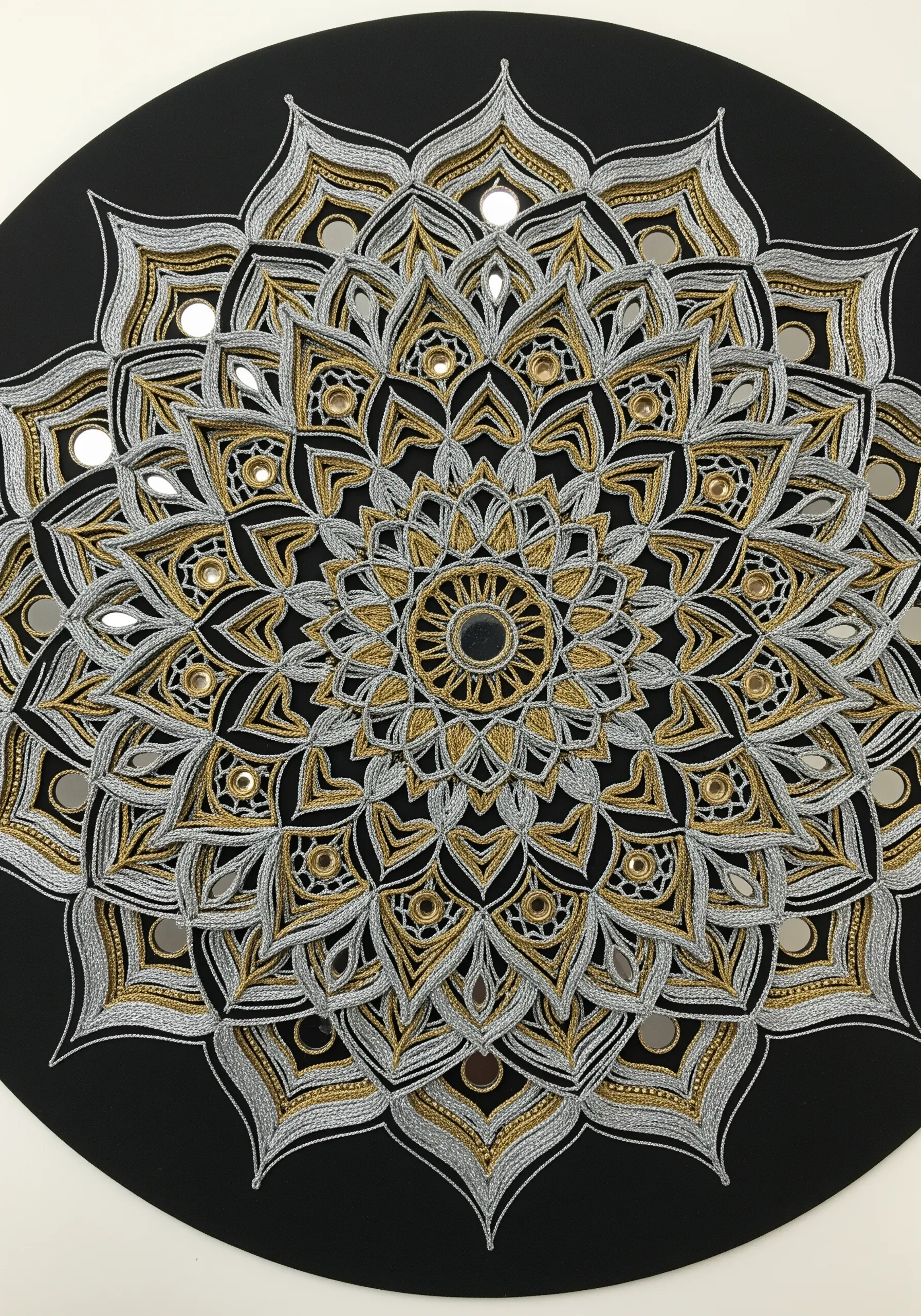 A complex black, silver, and gold mandala design featuring small, integrated mirrors.