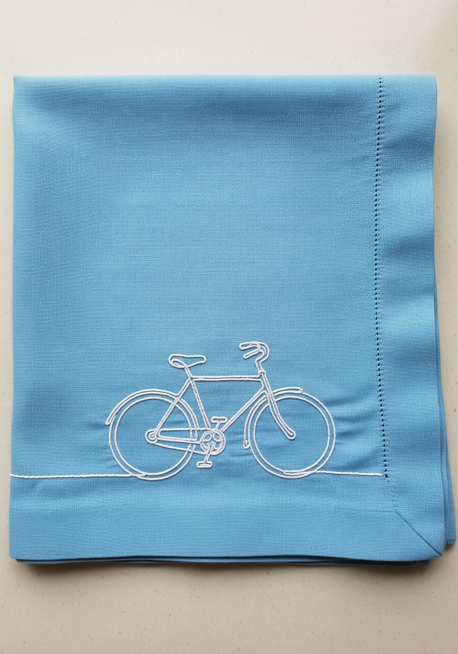 A detailed bicycle embroidered in white thread on a bright blue folded napkin.