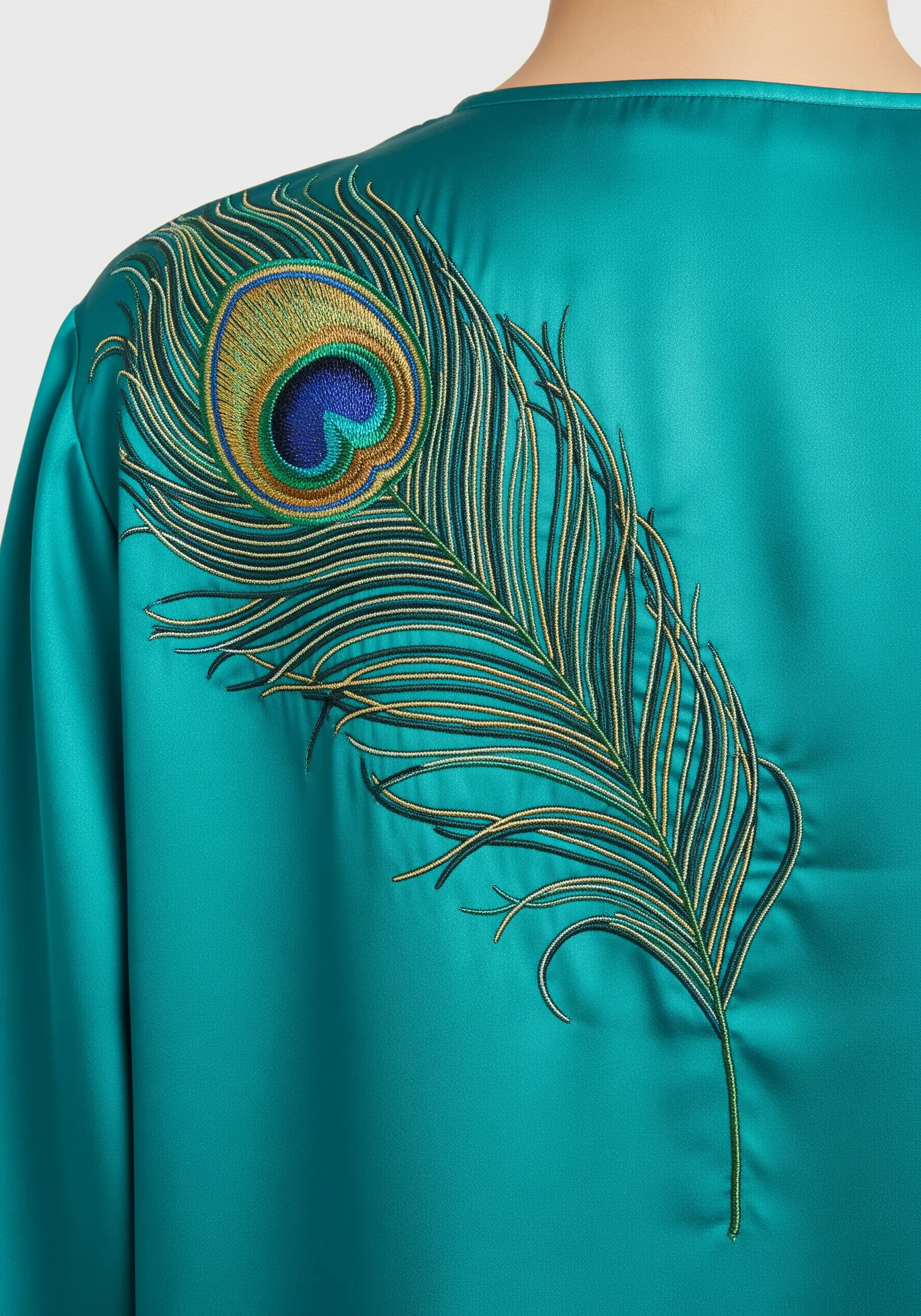 A single, intricately embroidered peacock feather on the shoulder of a teal satin blouse.
