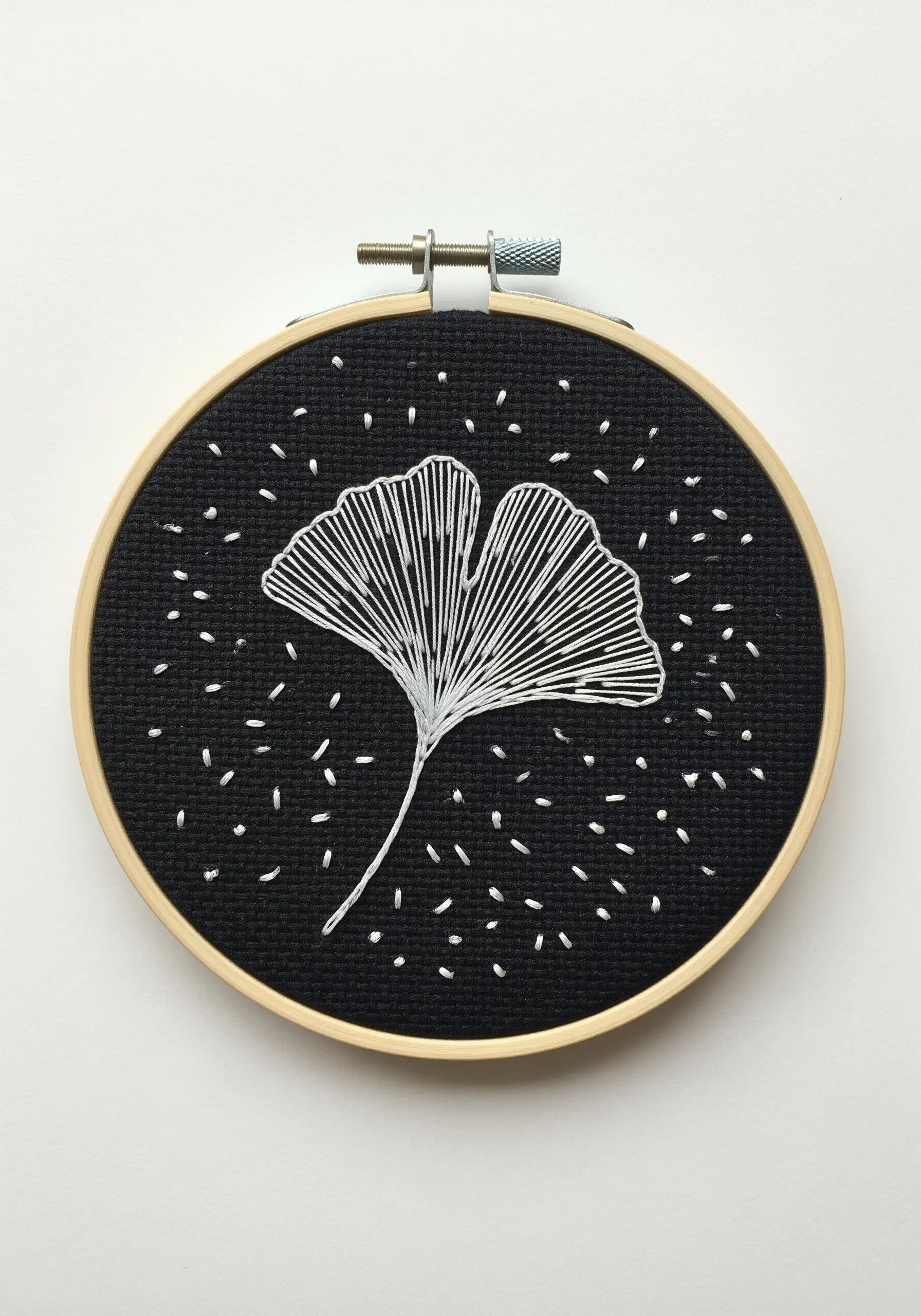 A ginkgo leaf stitched with radiating white lines on black fabric, creating a stark negative space.