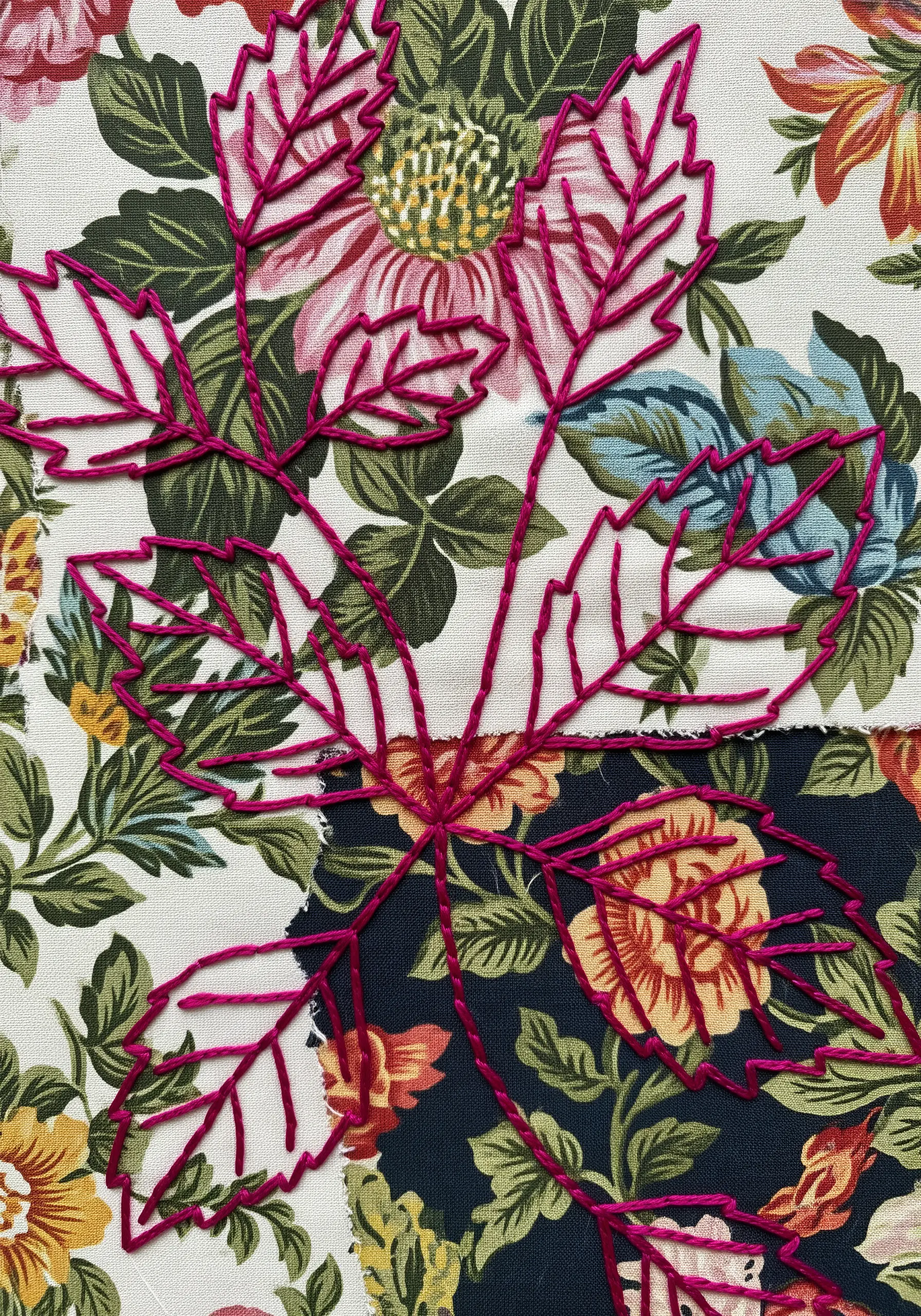 A magenta leaf outline stitched over two different floral patterned fabric pieces.