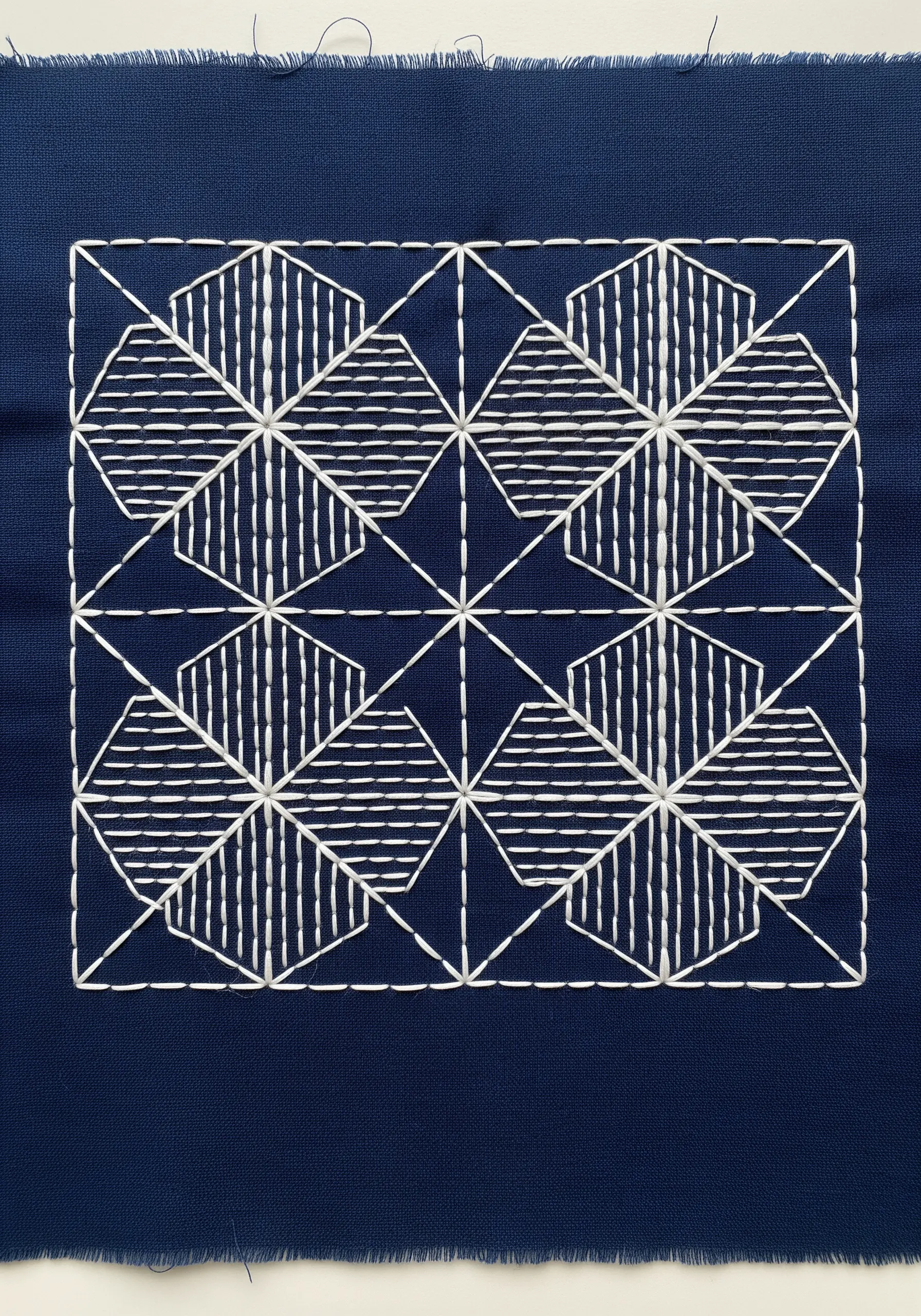 Close-up of a Japanese Sashiko pattern with white thread on dark blue fabric.