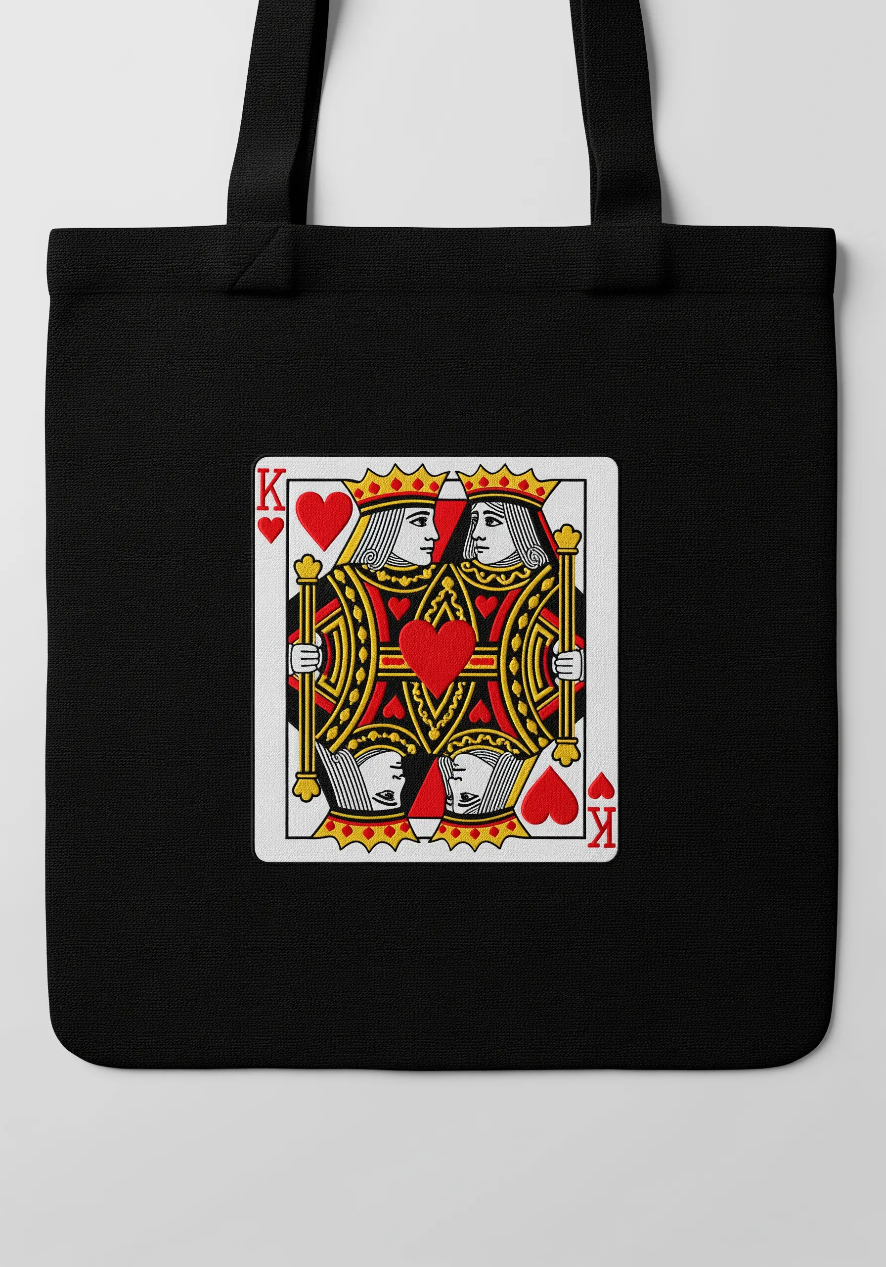 A detailed embroidery of a King of Hearts playing card on the front of a black tote bag.