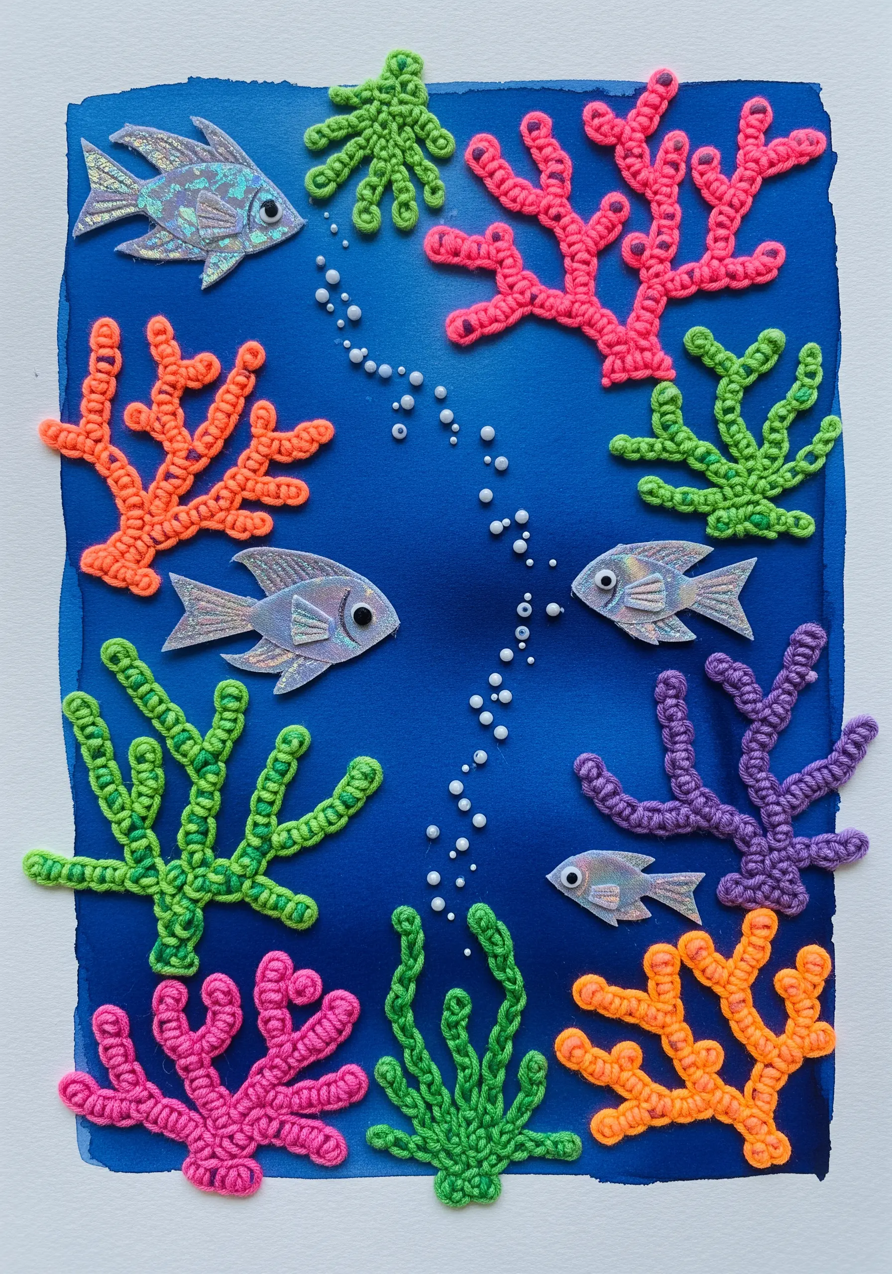 A mixed-media underwater scene with knotted cord coral and iridescent paper fish.