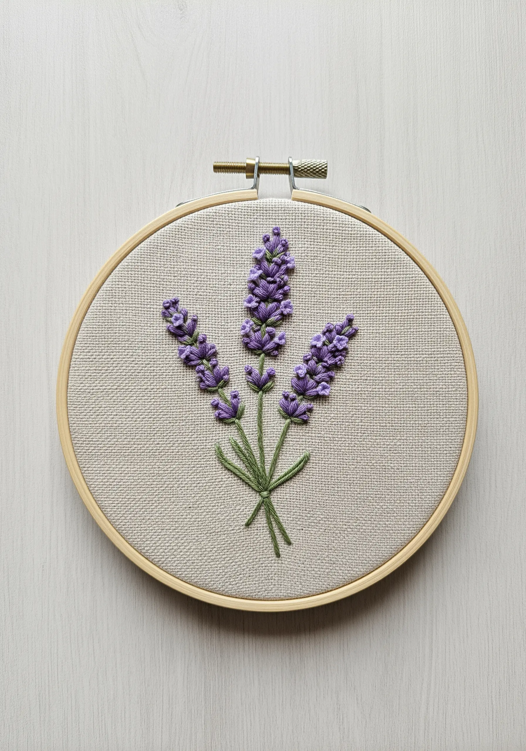 Embroidered lavender sprigs with purple French knots and green stems in a wooden hoop.