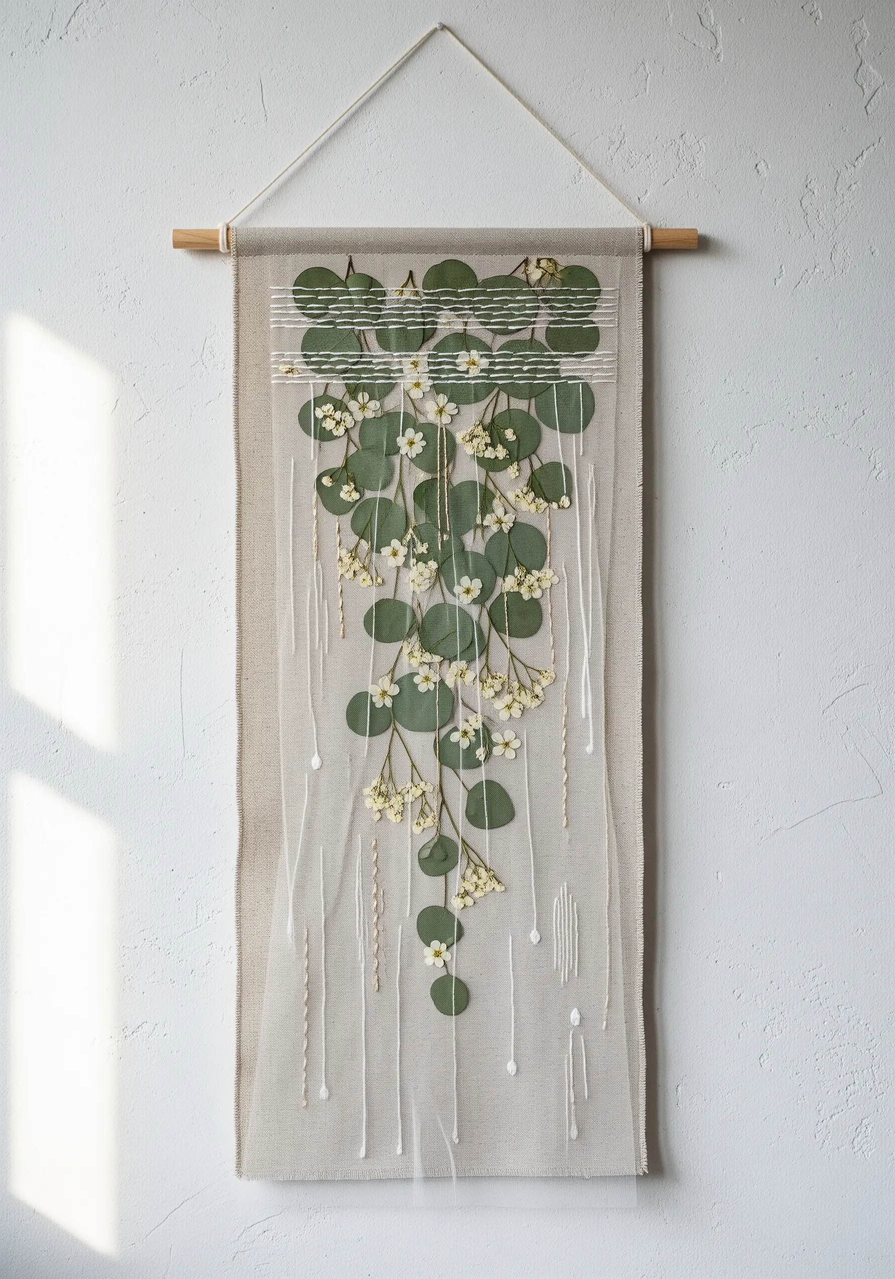 A wall hanging with pressed eucalyptus layered between a linen base and a sheer fabric overlay.