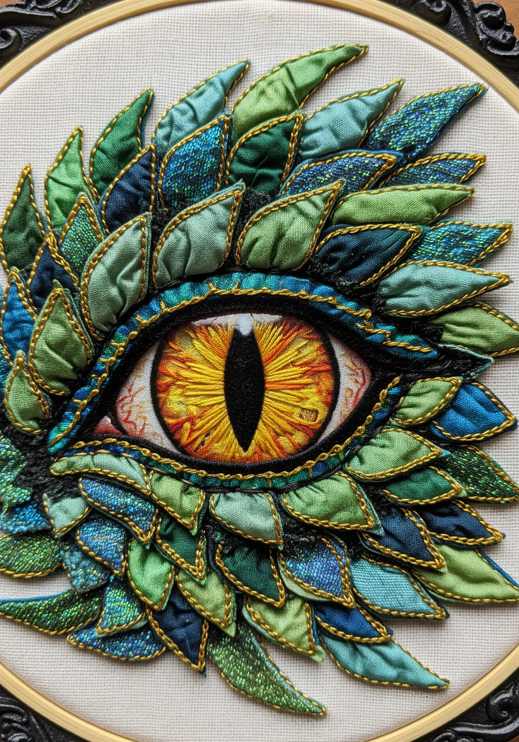 A close-up of a dragon's eye surrounded by layered, stitched fabric scales in green and blue.