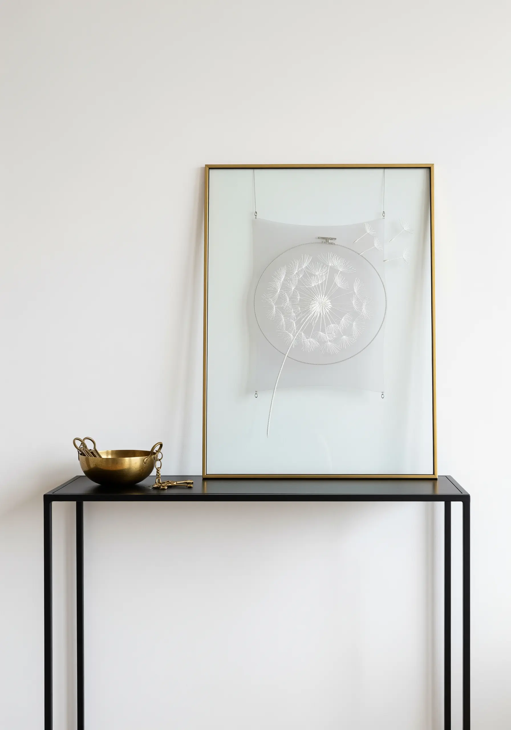 A dandelion embroidered with white thread on sheer fabric inside a hoop.