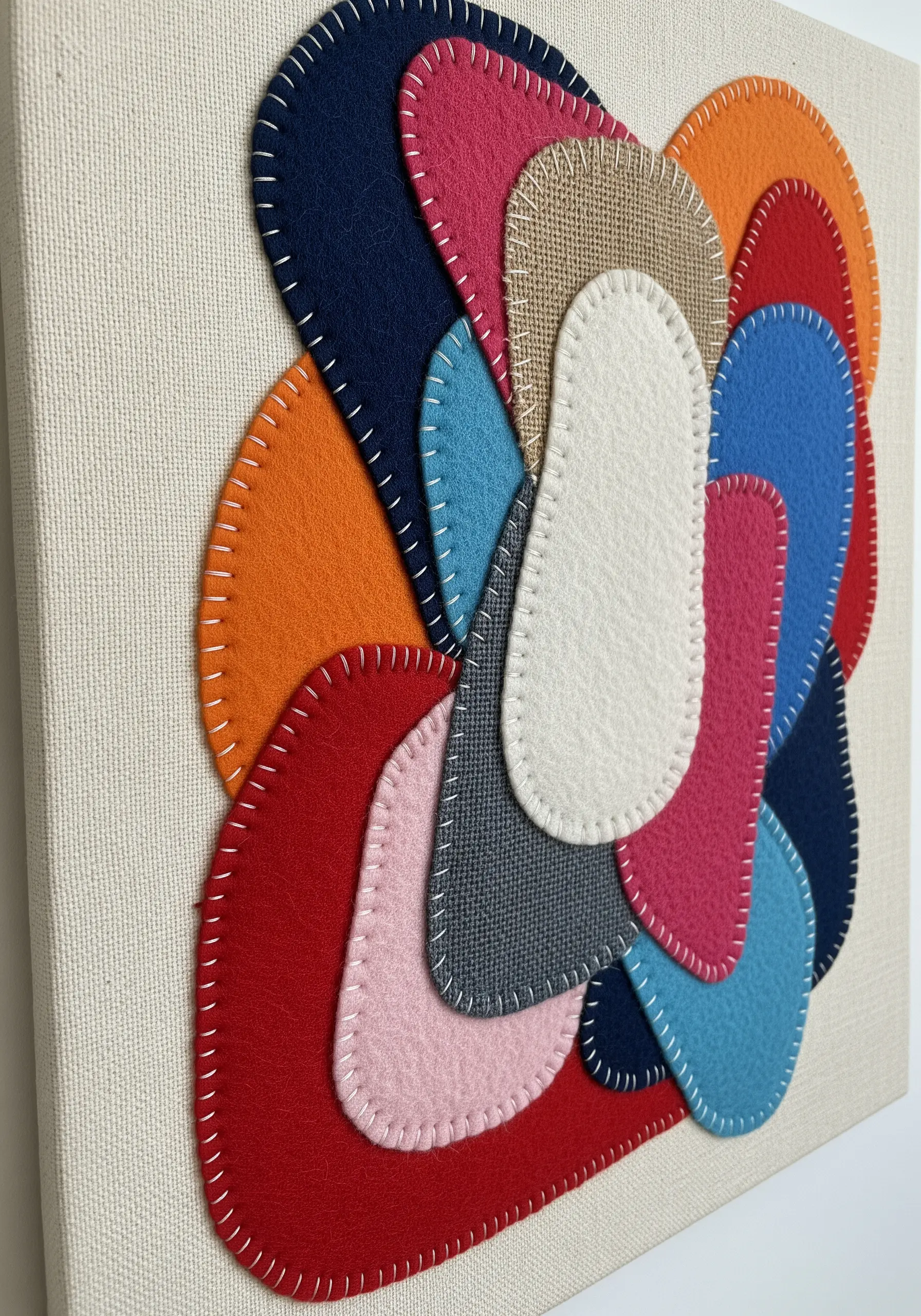 A colorful collage of layered felt shapes secured with a visible white whipstitch.