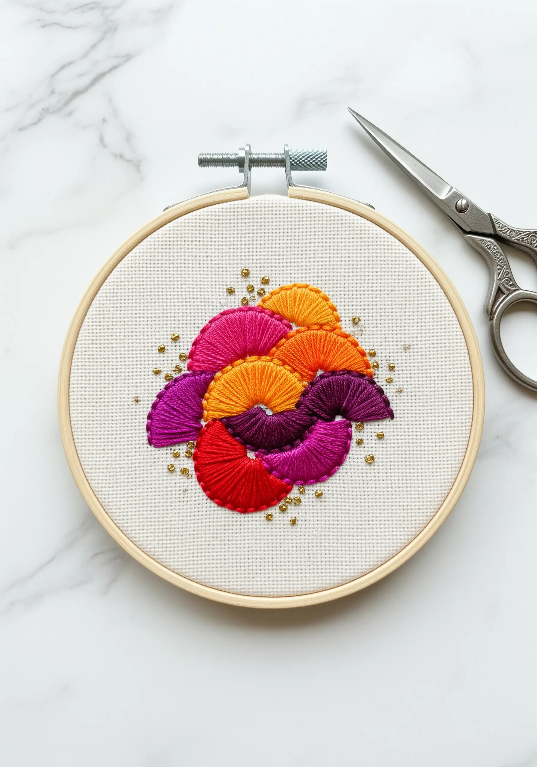 Overlapping fan-shaped satin stitches in bright colors with gold bead accents.