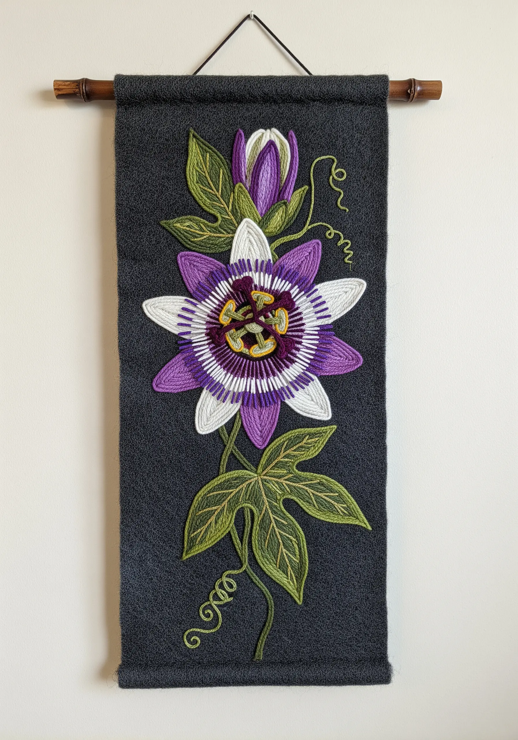 A complex passion flower embroidered on a dark grey felt wall hanging with 3D elements.