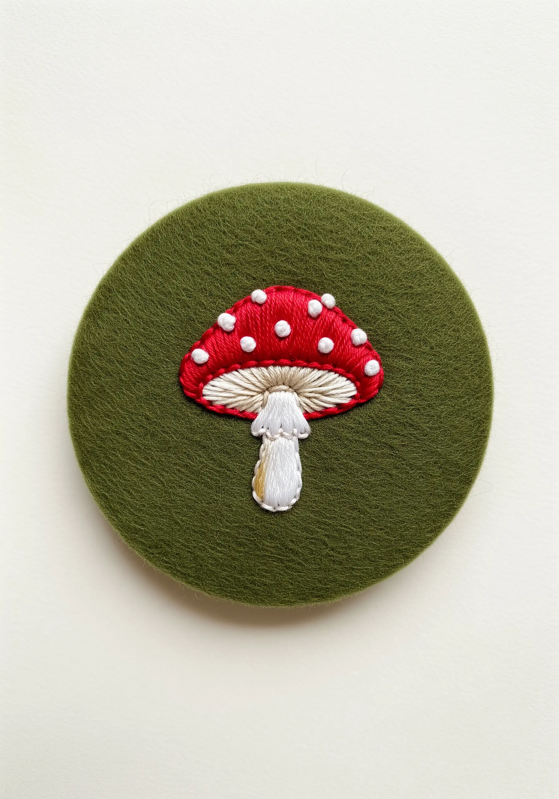 An embroidered red and white toadstool mushroom on a green felt background.