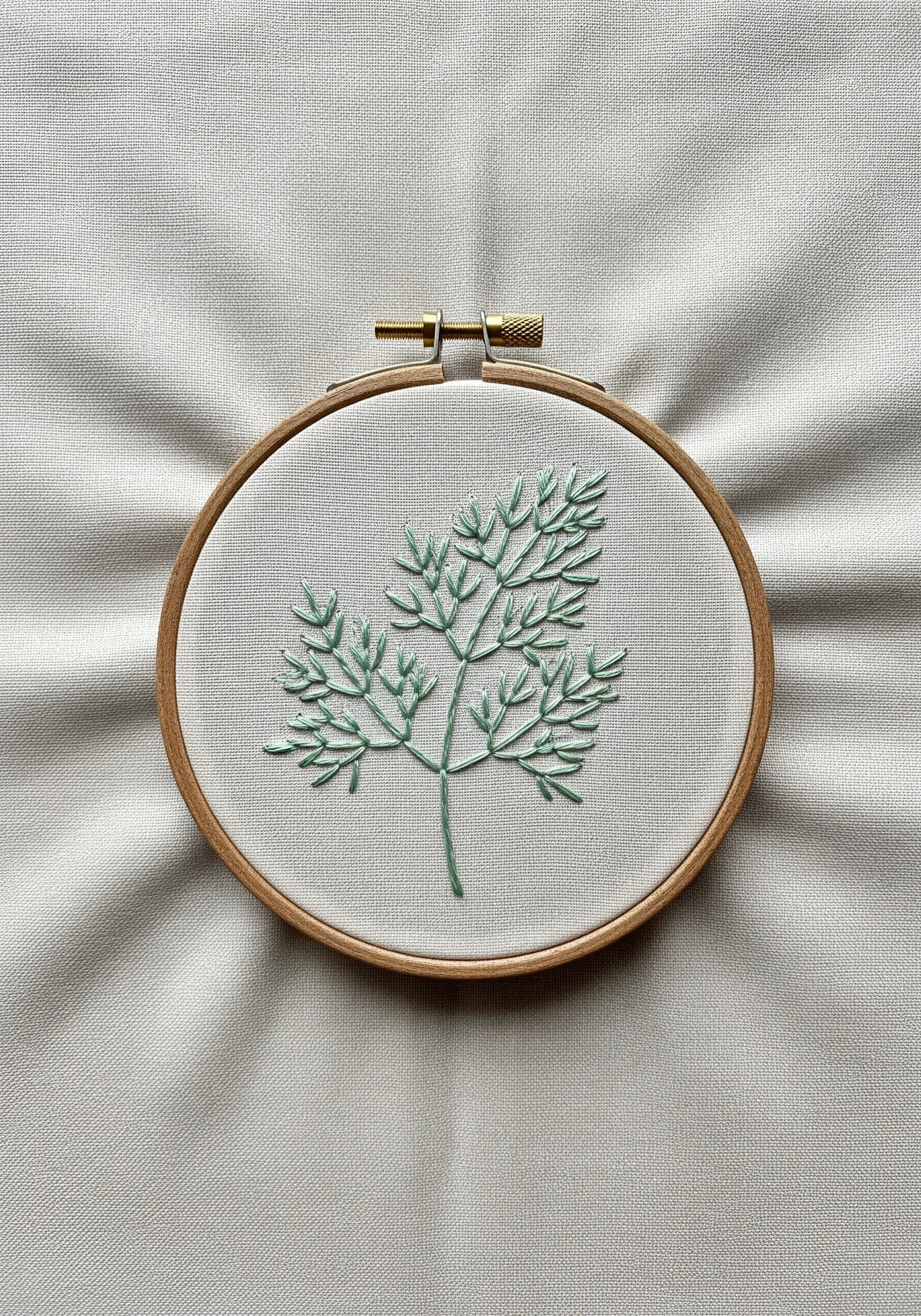 A sprig of dill embroidered in pale aqua-green, emphasizing the empty space within the hoop.