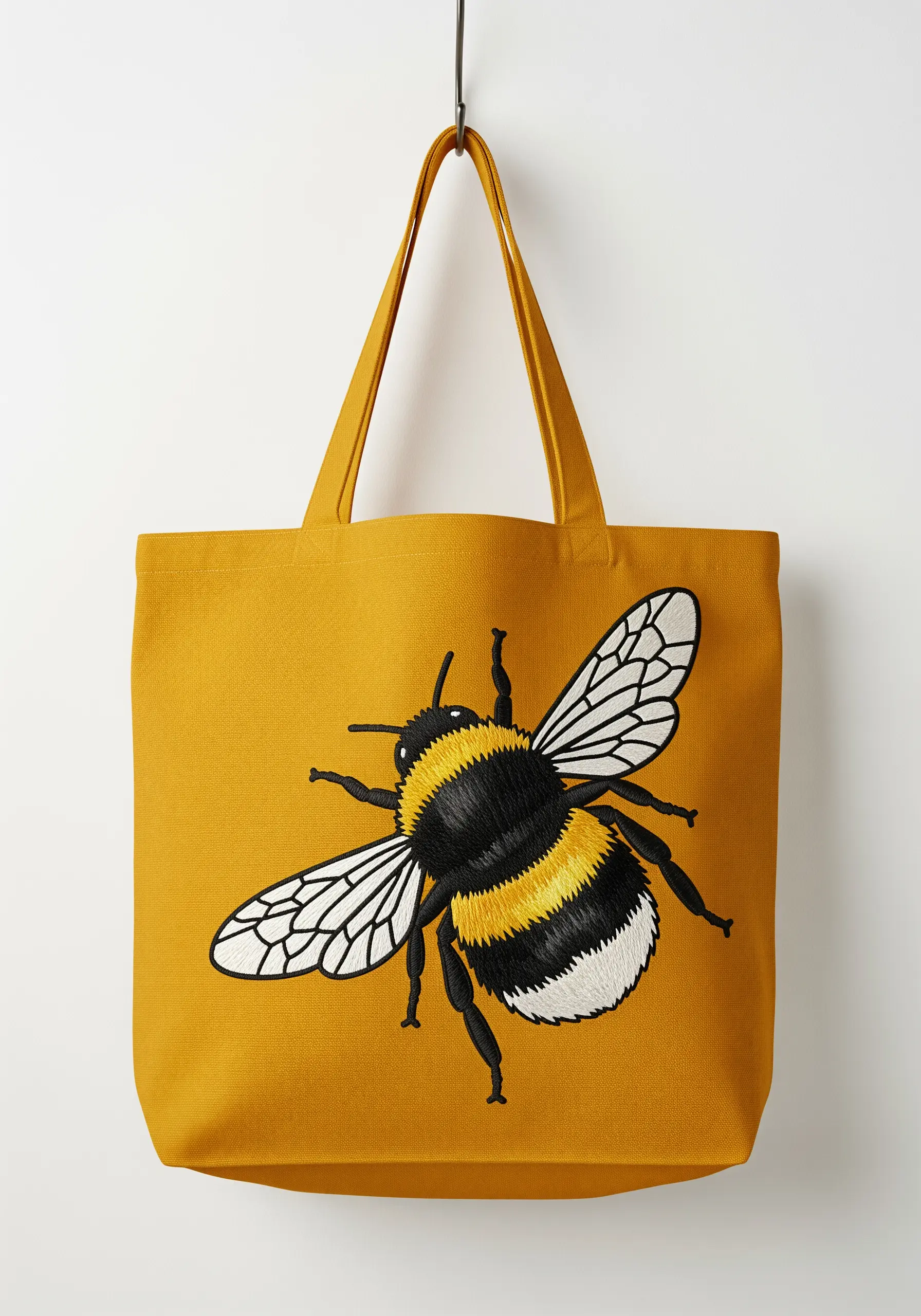 A large, realistically embroidered bee with fuzzy texture on a yellow tote bag.