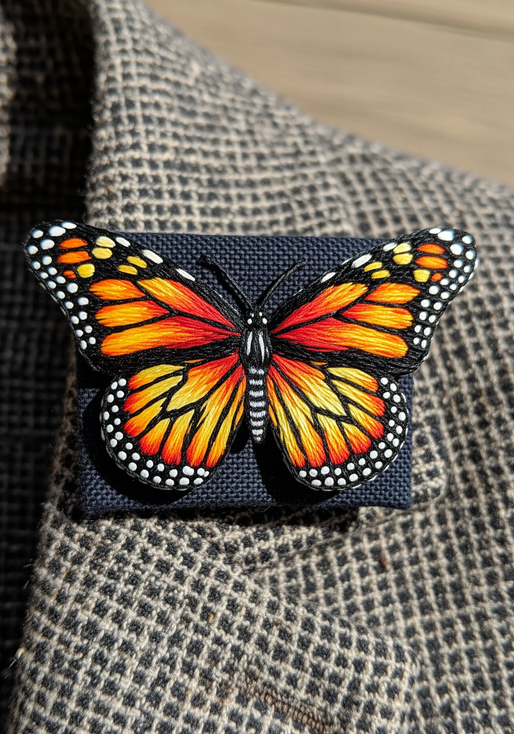 A realistic monarch butterfly brooch created with detailed thread painting and stumpwork techniques.
