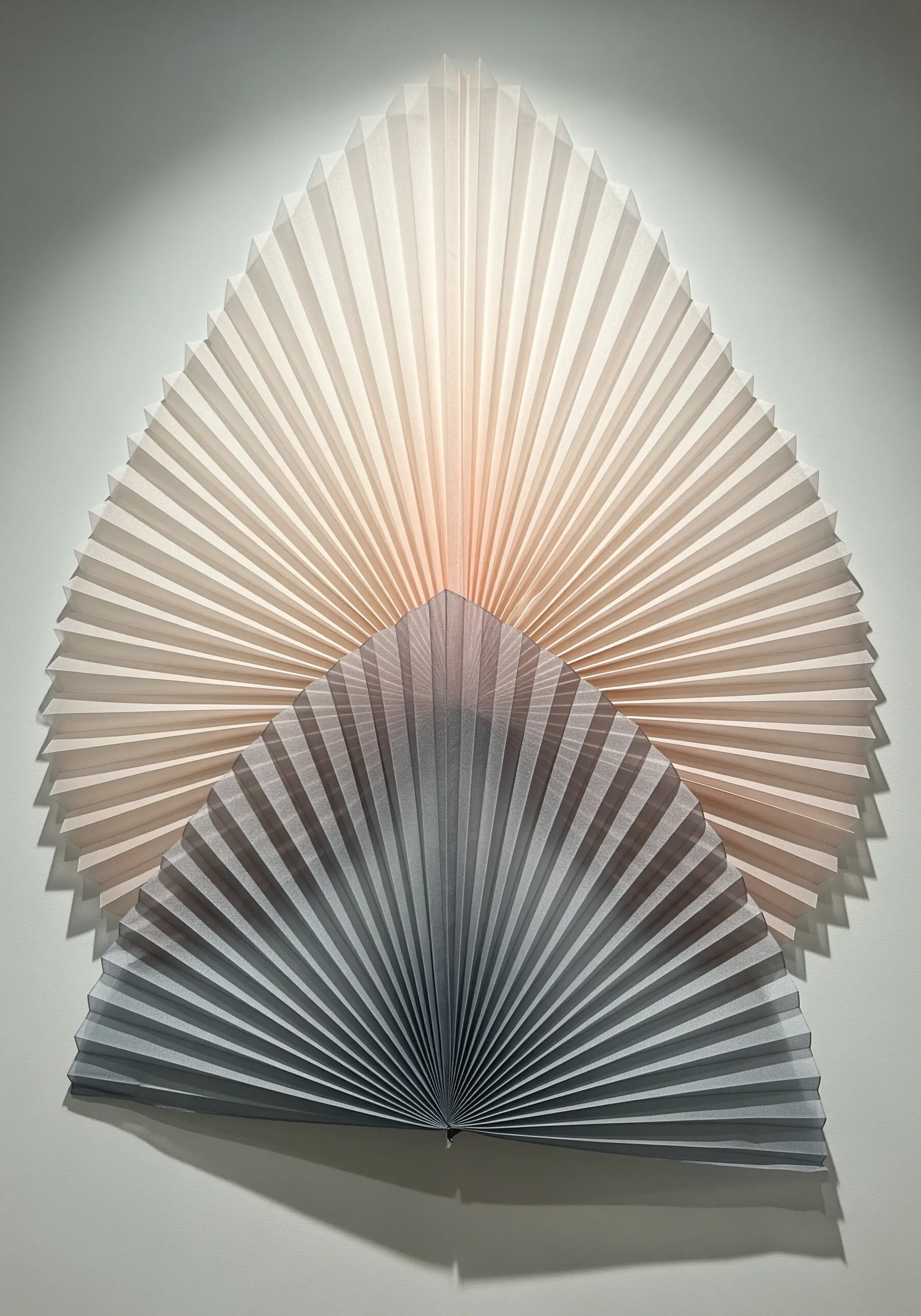 Two fanned-out sculptures made of precisely pleated paper, one light and one dark.
