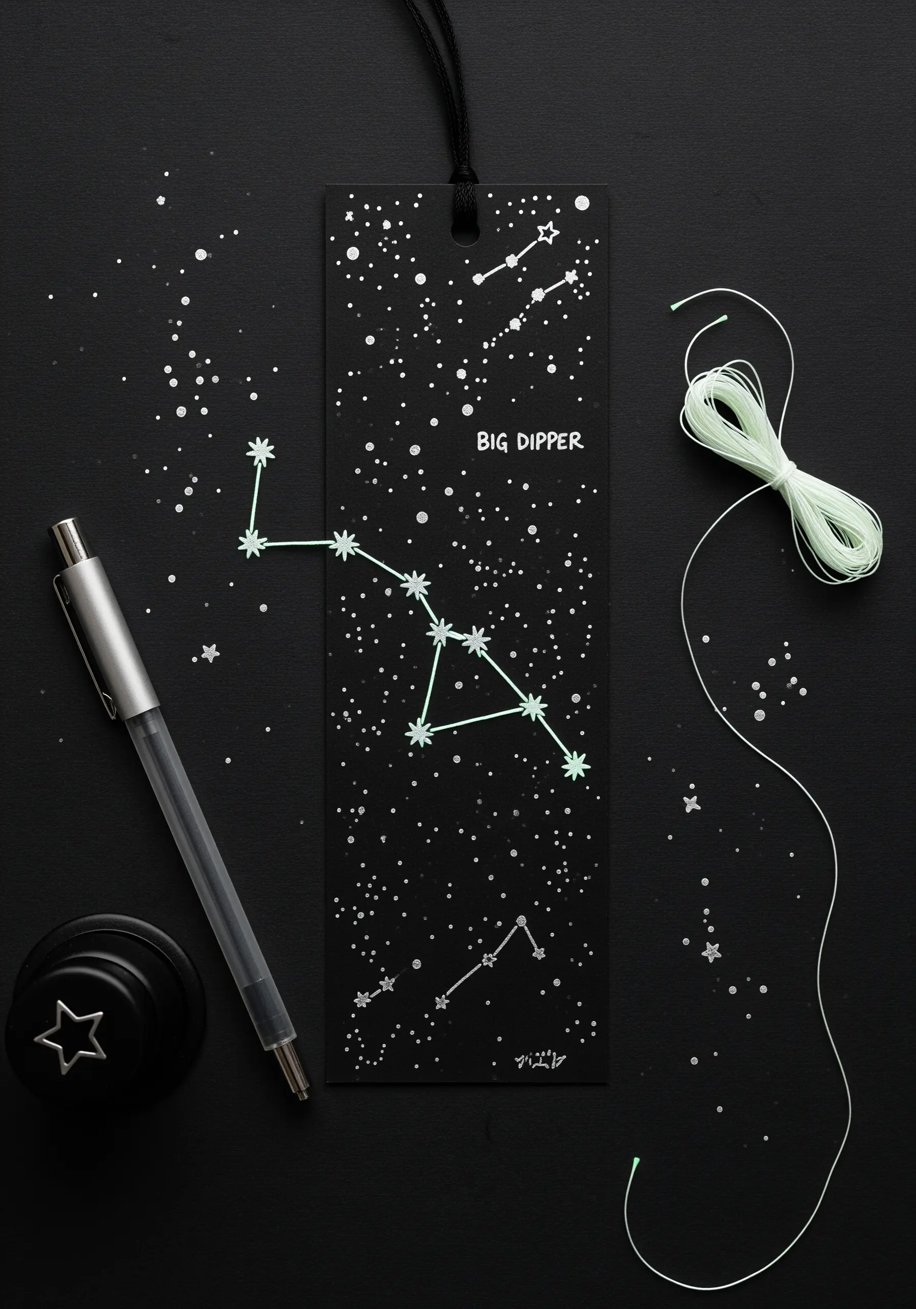 Big Dipper constellation embroidered with glow-in-the-dark thread on a black paper bookmark.